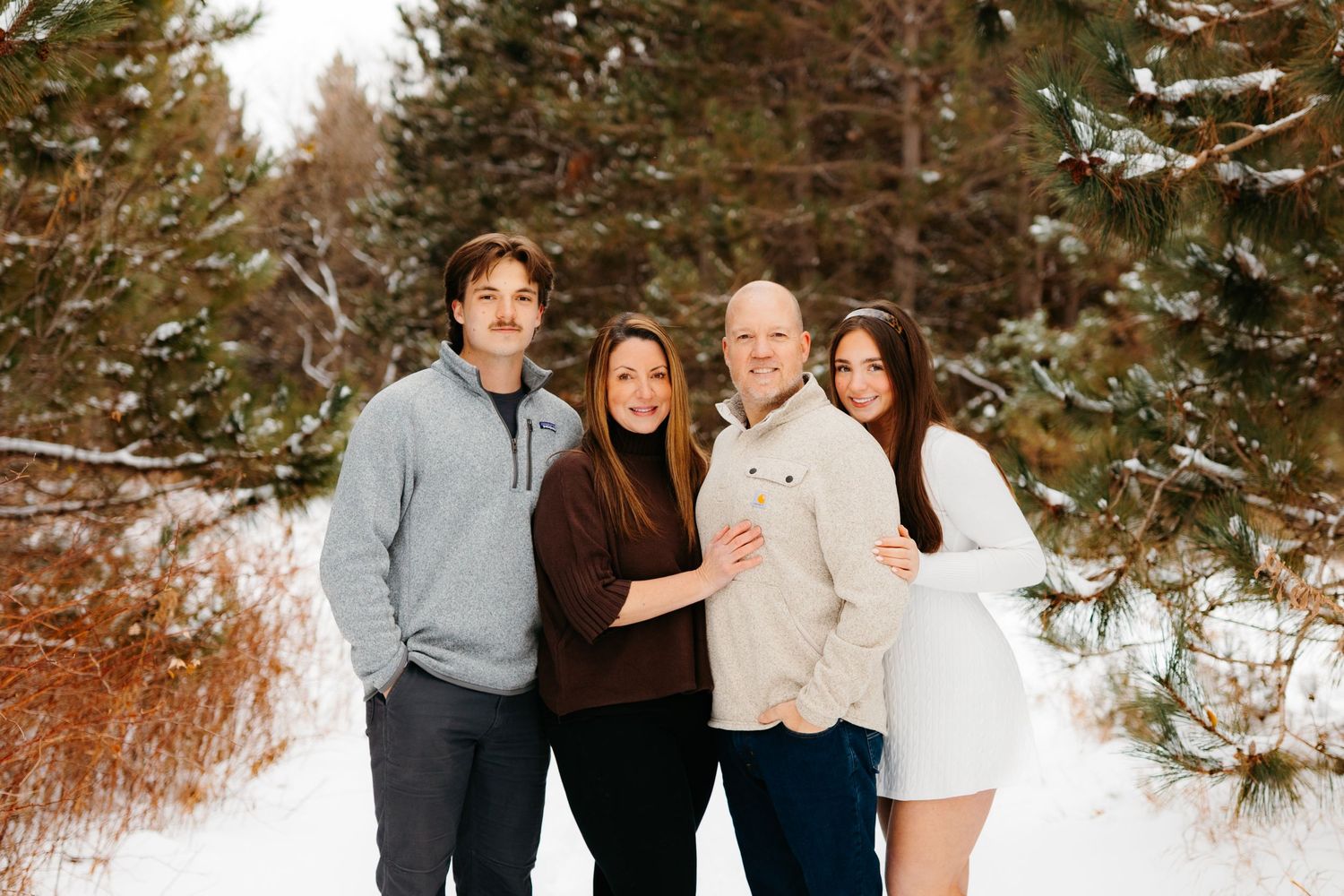 Family group poses together in snowy winter setting with evergreen trees.