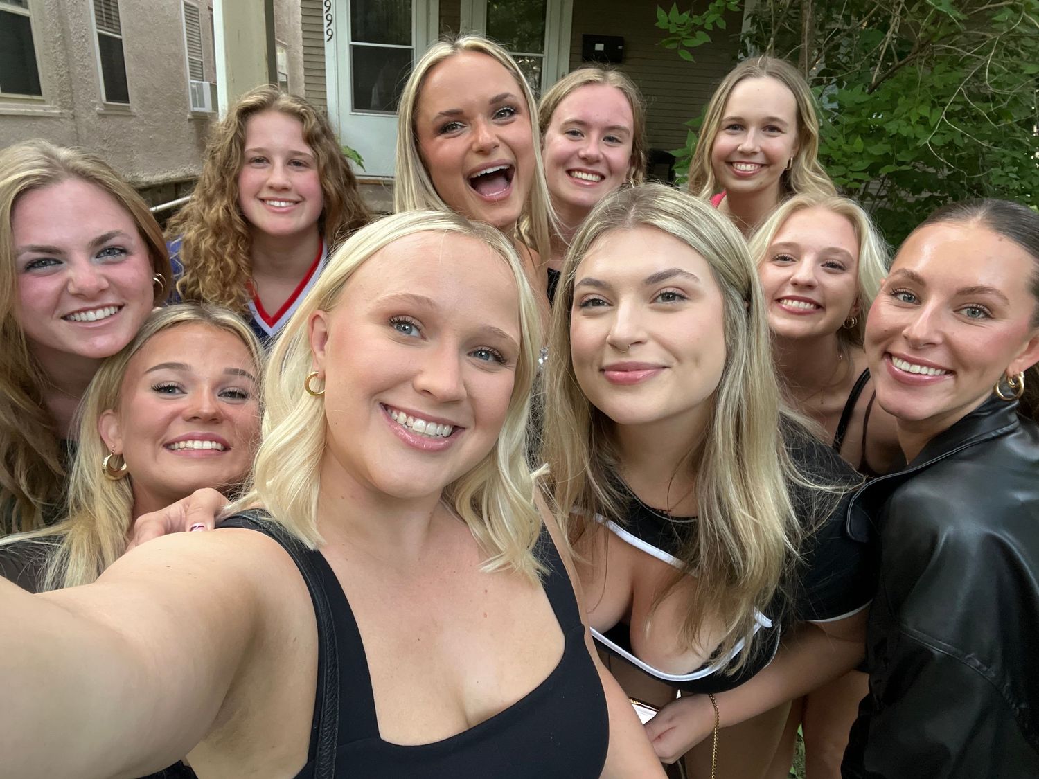 Group selfie of friends in black outfits smiling together outdoors.