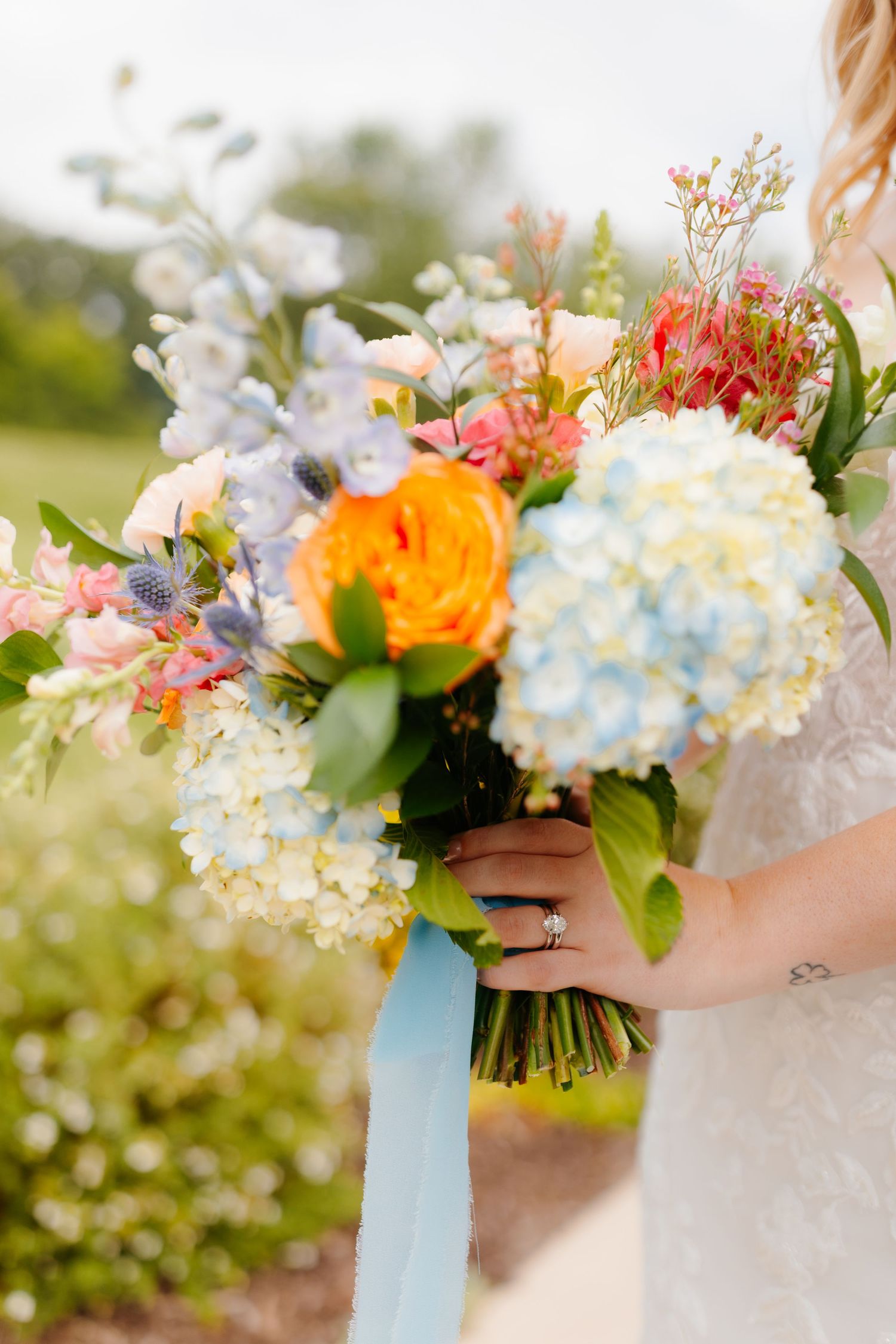 Vibrant bridal bouquet features hydrangeas, roses and delicate flowers tied with blue ribbon.