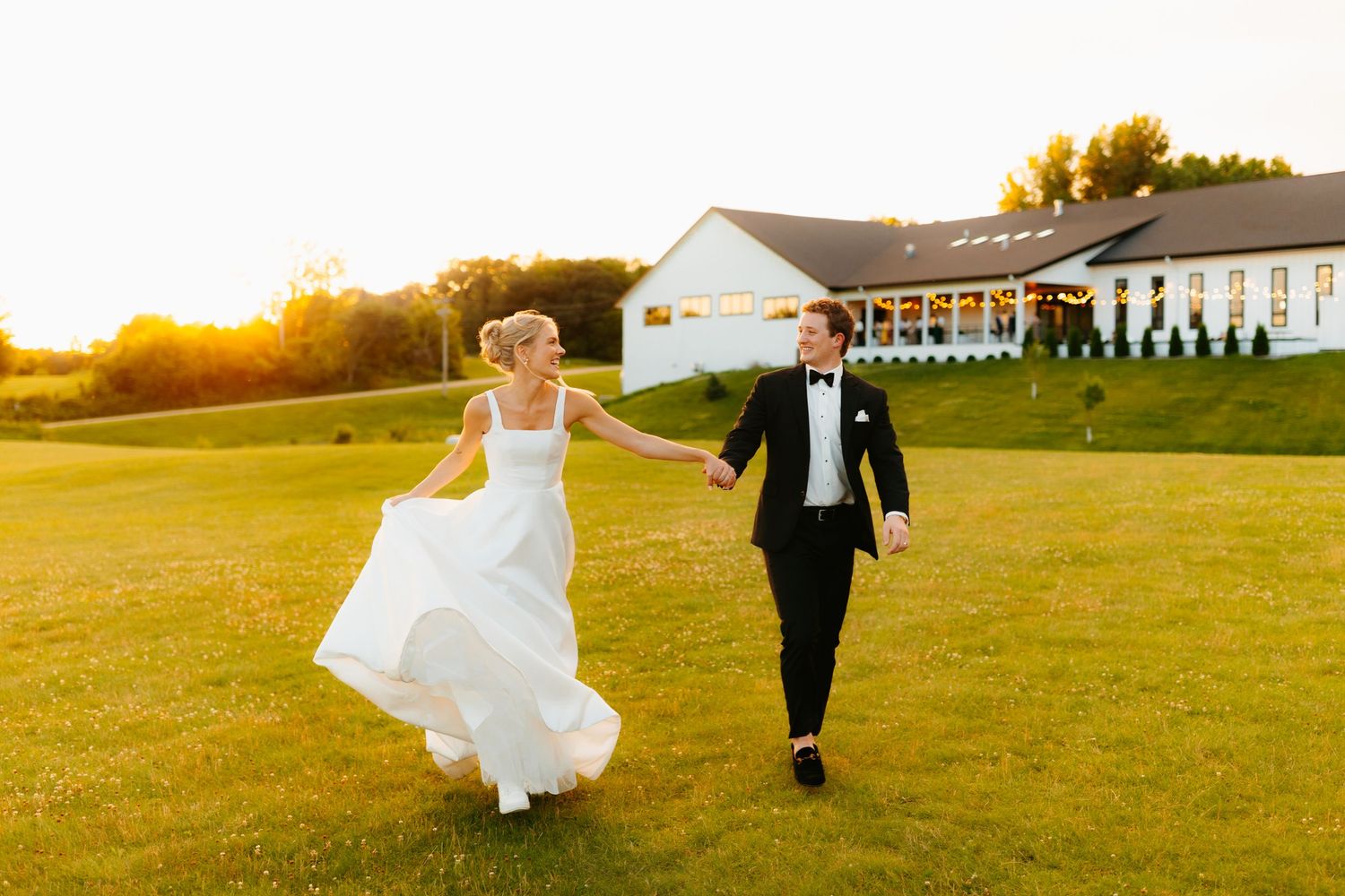 Couple running playfully across grassy field at sunset.