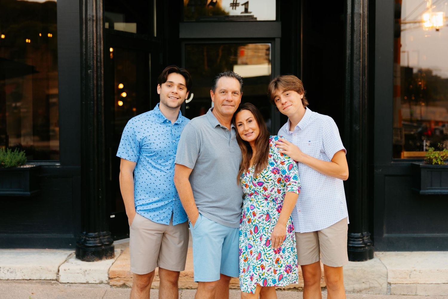 Small group gathers for casual photo outside storefront in evening.