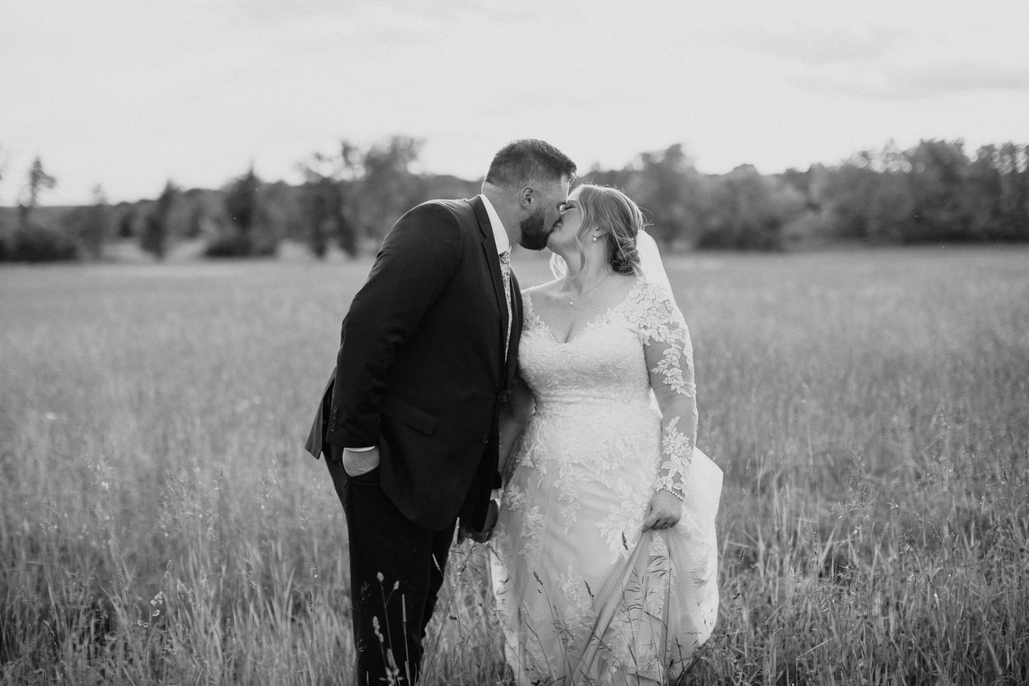 Romantic couple walks through a serene meadow at sunset in black and white photography.