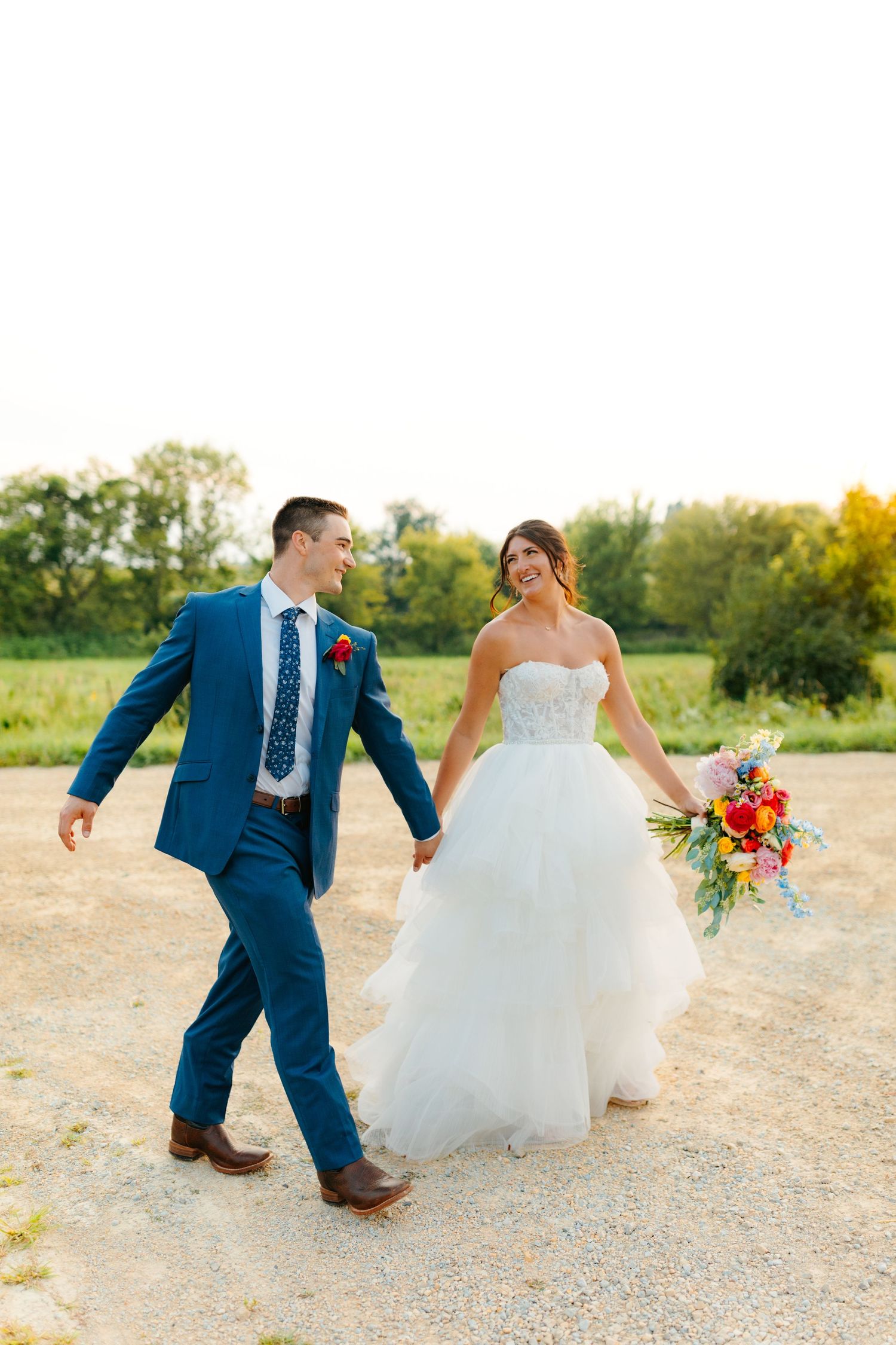 Newlyweds dance and twirl together on a country path during their wedding photoshoot.