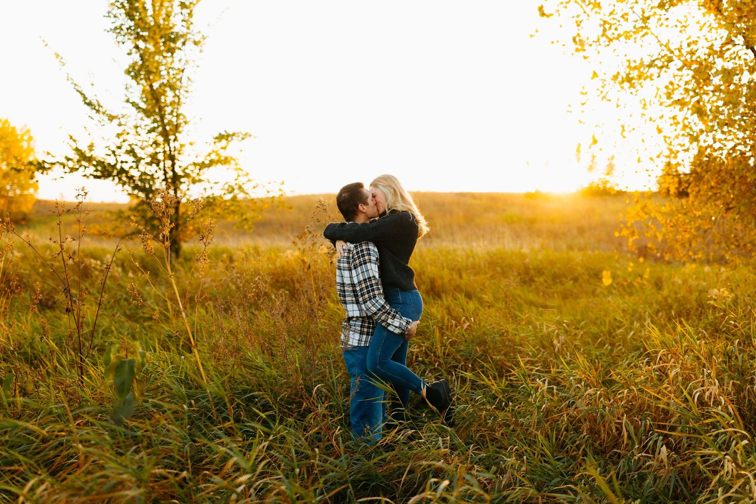 Romantic couple embraces in golden field during sunset photoshoot.