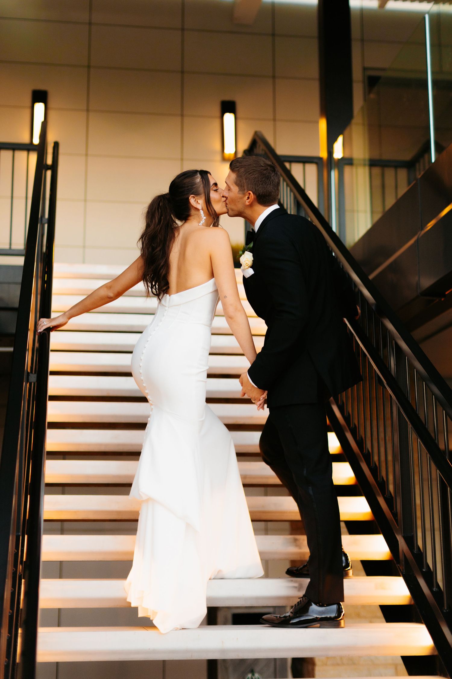 Romantic couple ascending illuminated stairs in wedding attire.