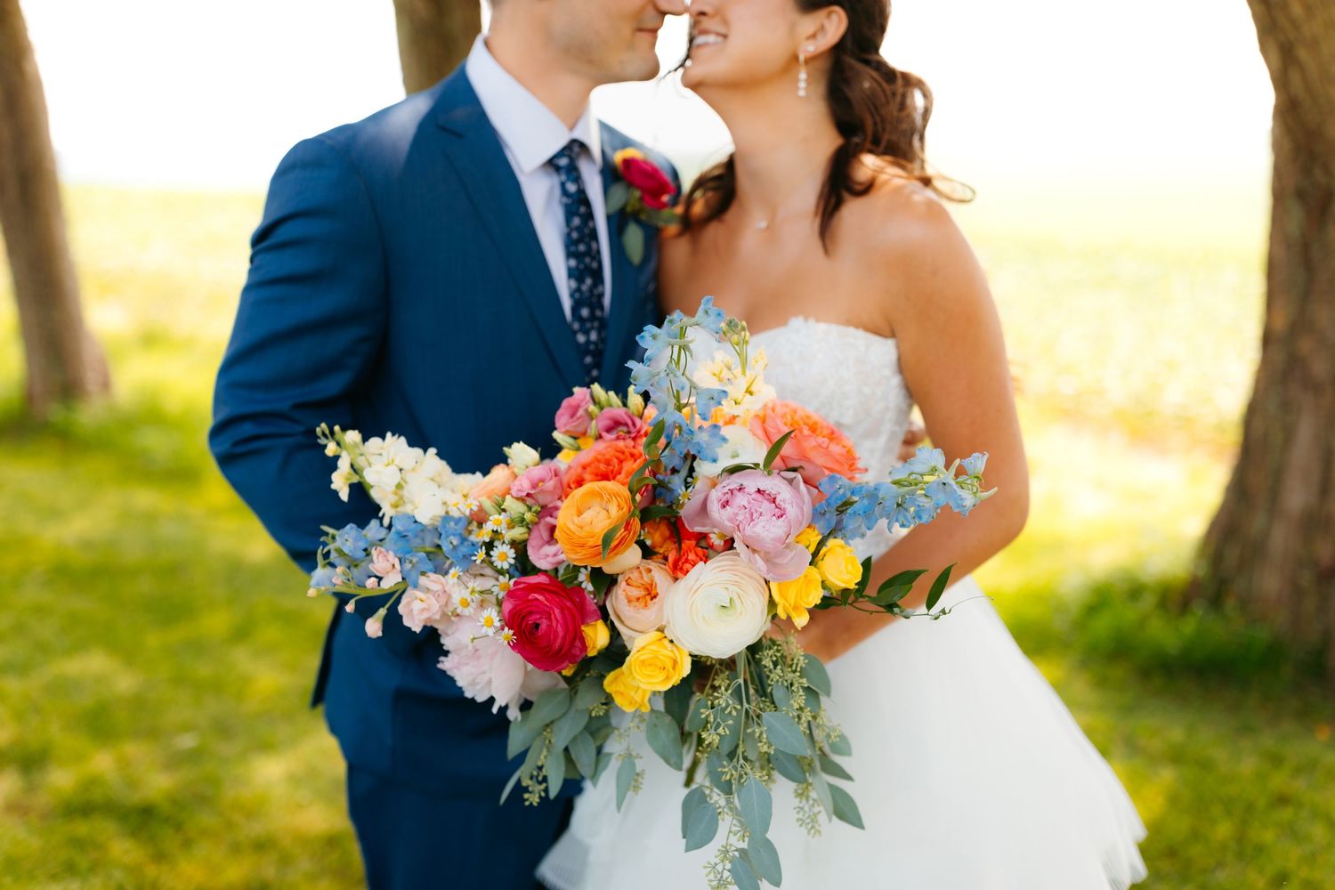Colorful wedding bouquet with pink and yellow flowers against navy blue attire.