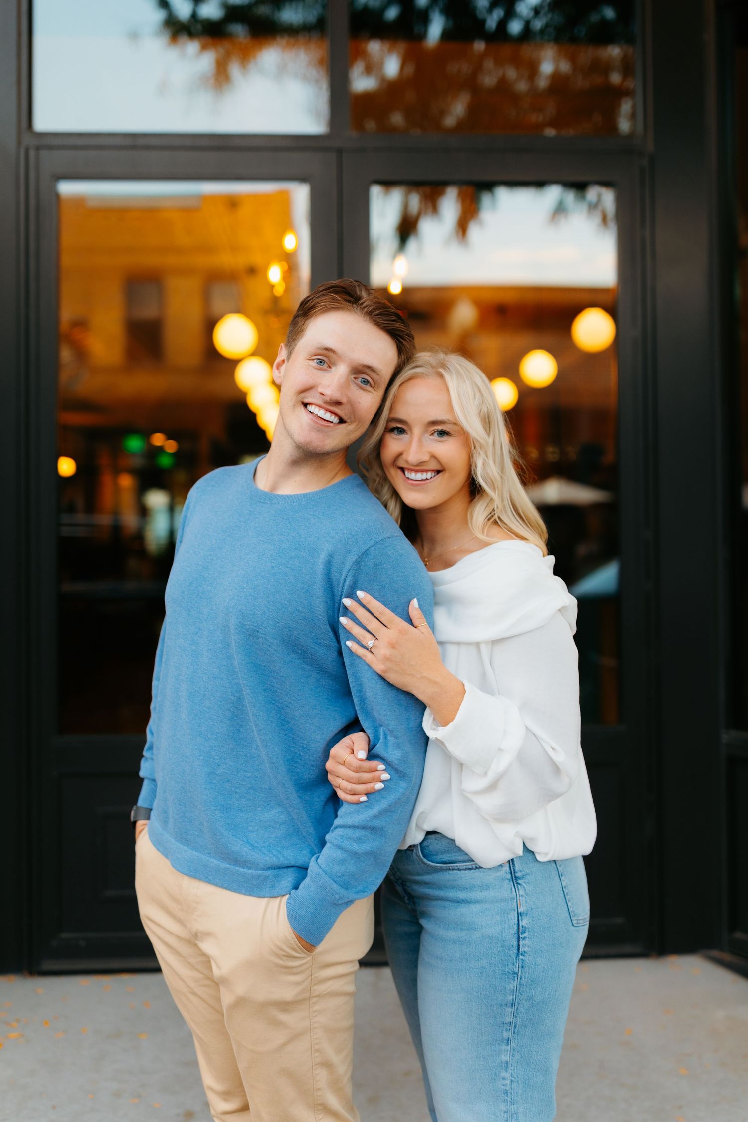 Couple in casual winter outfits embracing outside storefront at dusk.