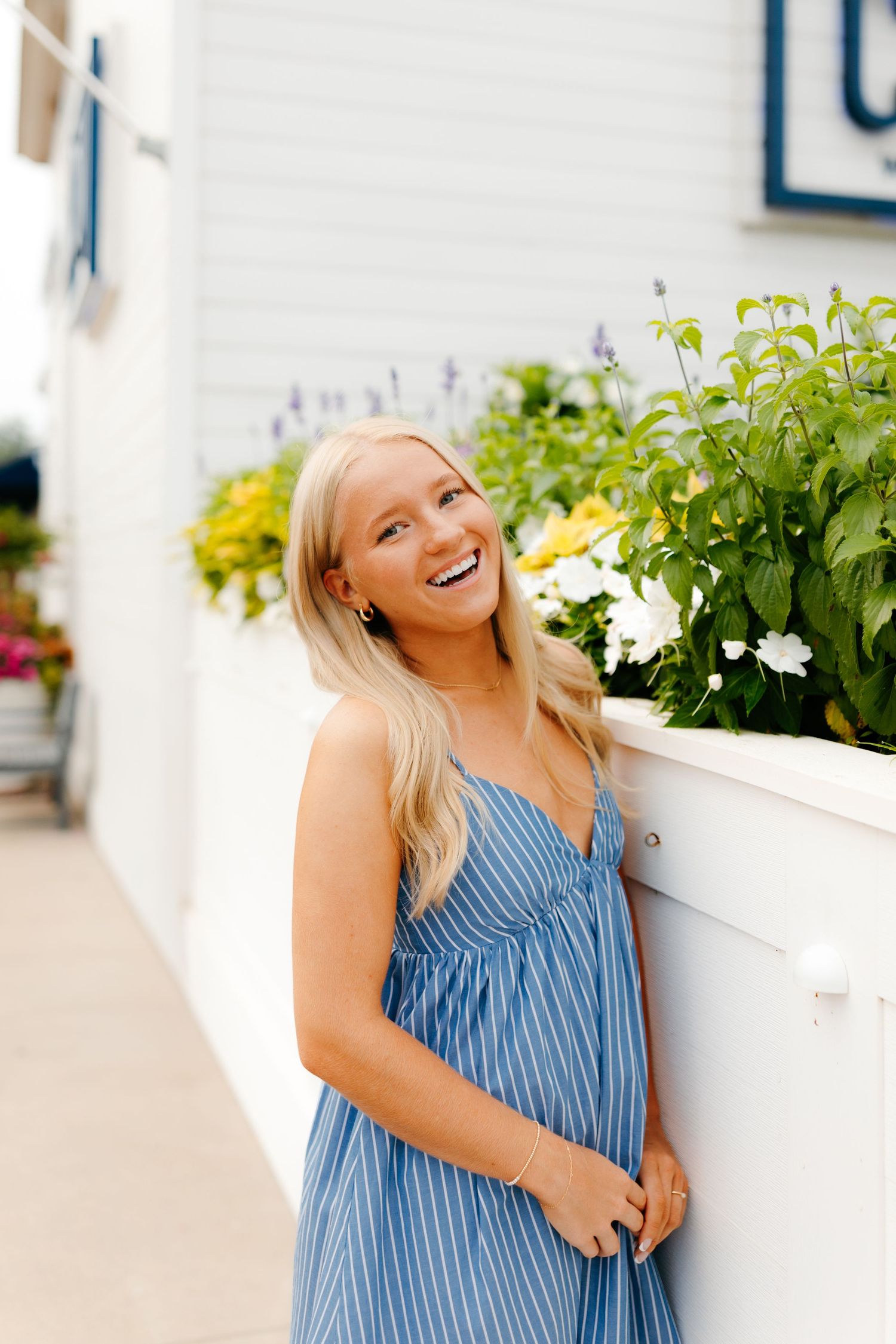Blue striped sundress styled against white architectural backdrop with flowering plants.