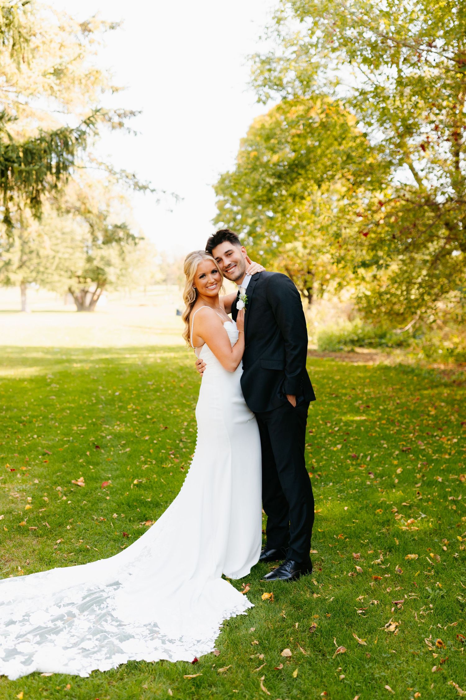 Elegant wedding couple embraces on green lawn during golden hour photography session.