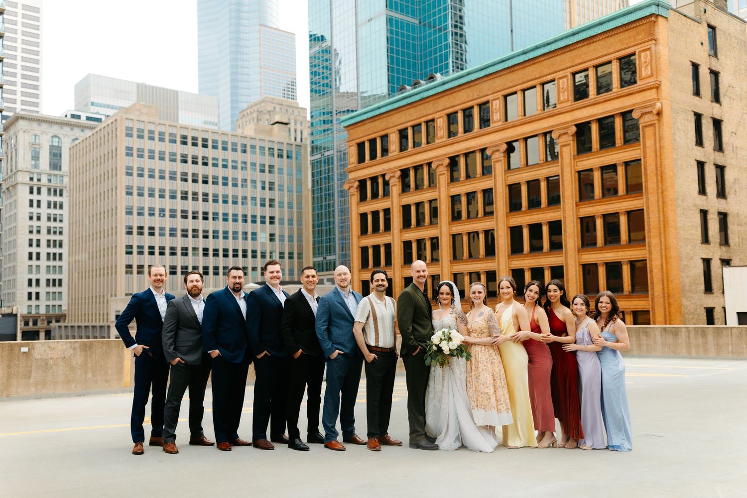 Wedding party poses together on urban rooftop with historic brick buildings and modern skyscrapers in background.