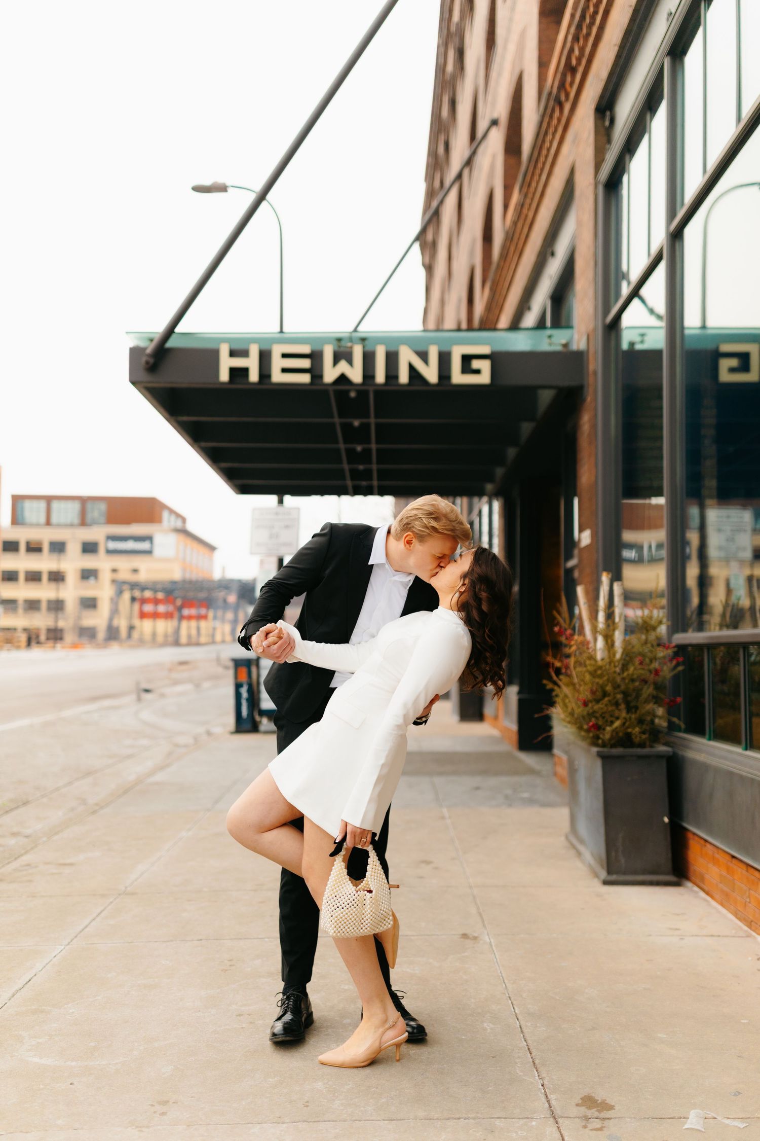 Stylish couple in black and white outfits posing playfully on city sidewalk.
