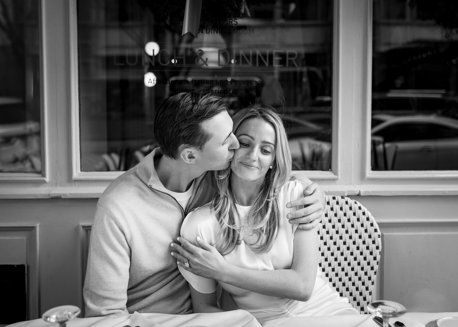 Black and white photo of a couple sharing a tender kiss at an outdoor cafe.