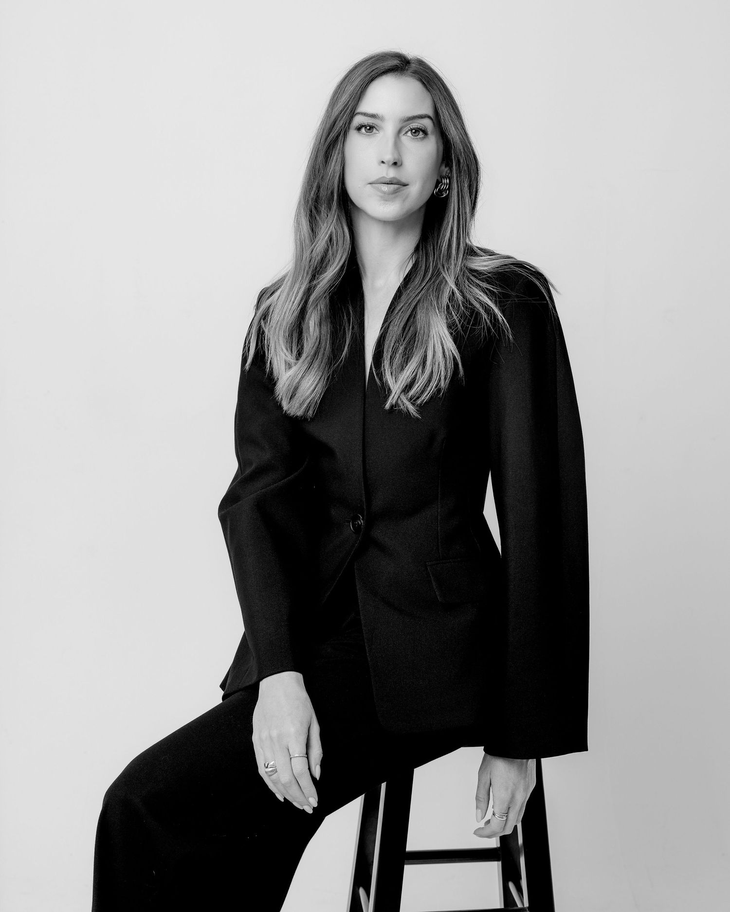 Black and white portrait of a woman in a black blazer seated on a stool.