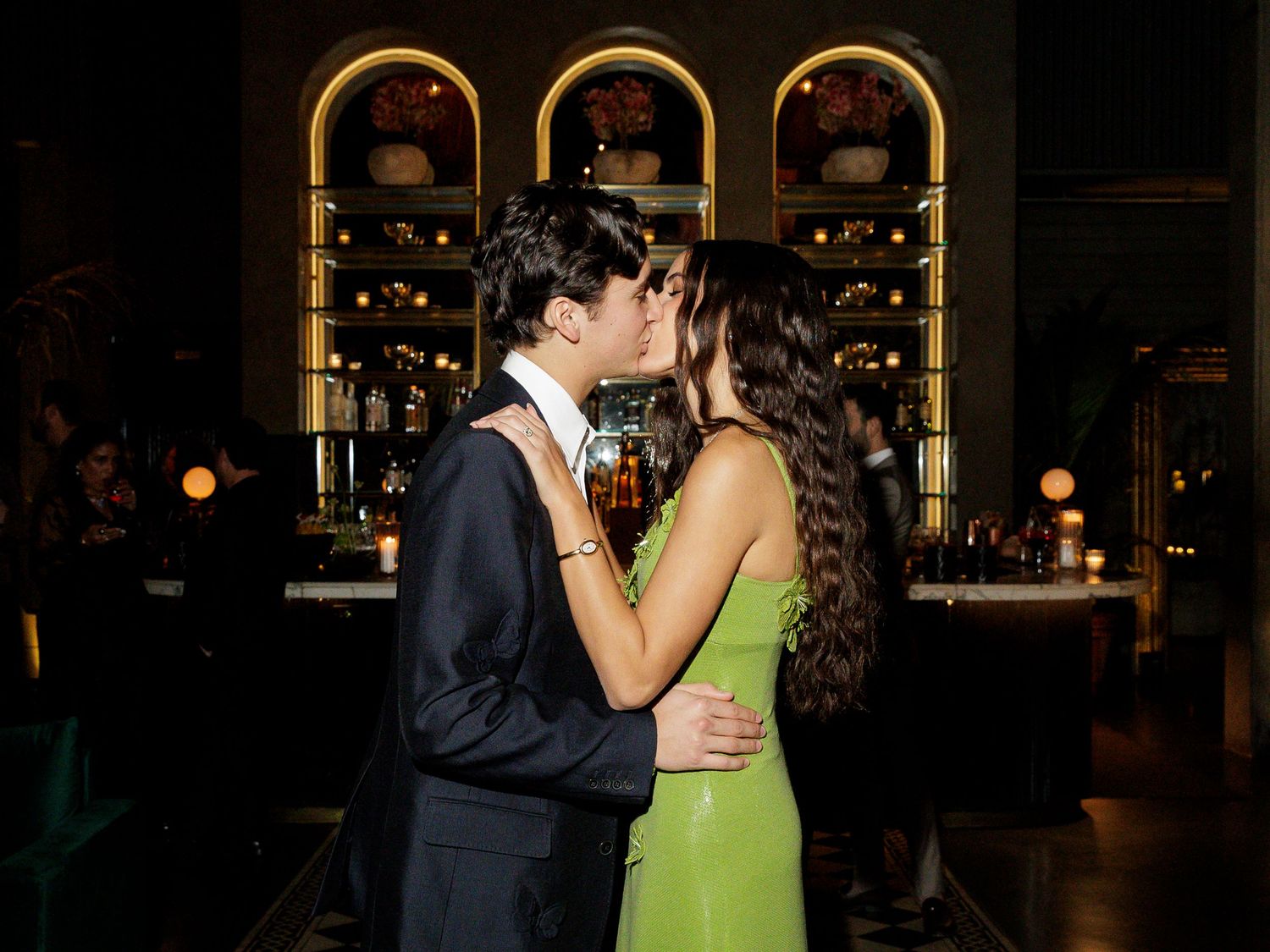 Couple shares a romantic kiss at an upscale bar, woman in elegant green gown.