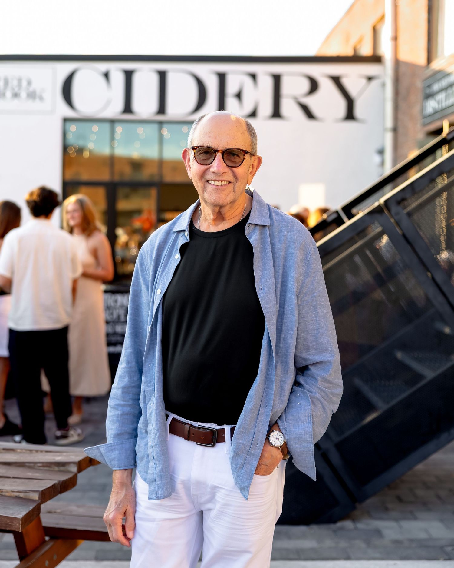 Stylish older man in casual attire standing outside a cidery on a sunny evening.