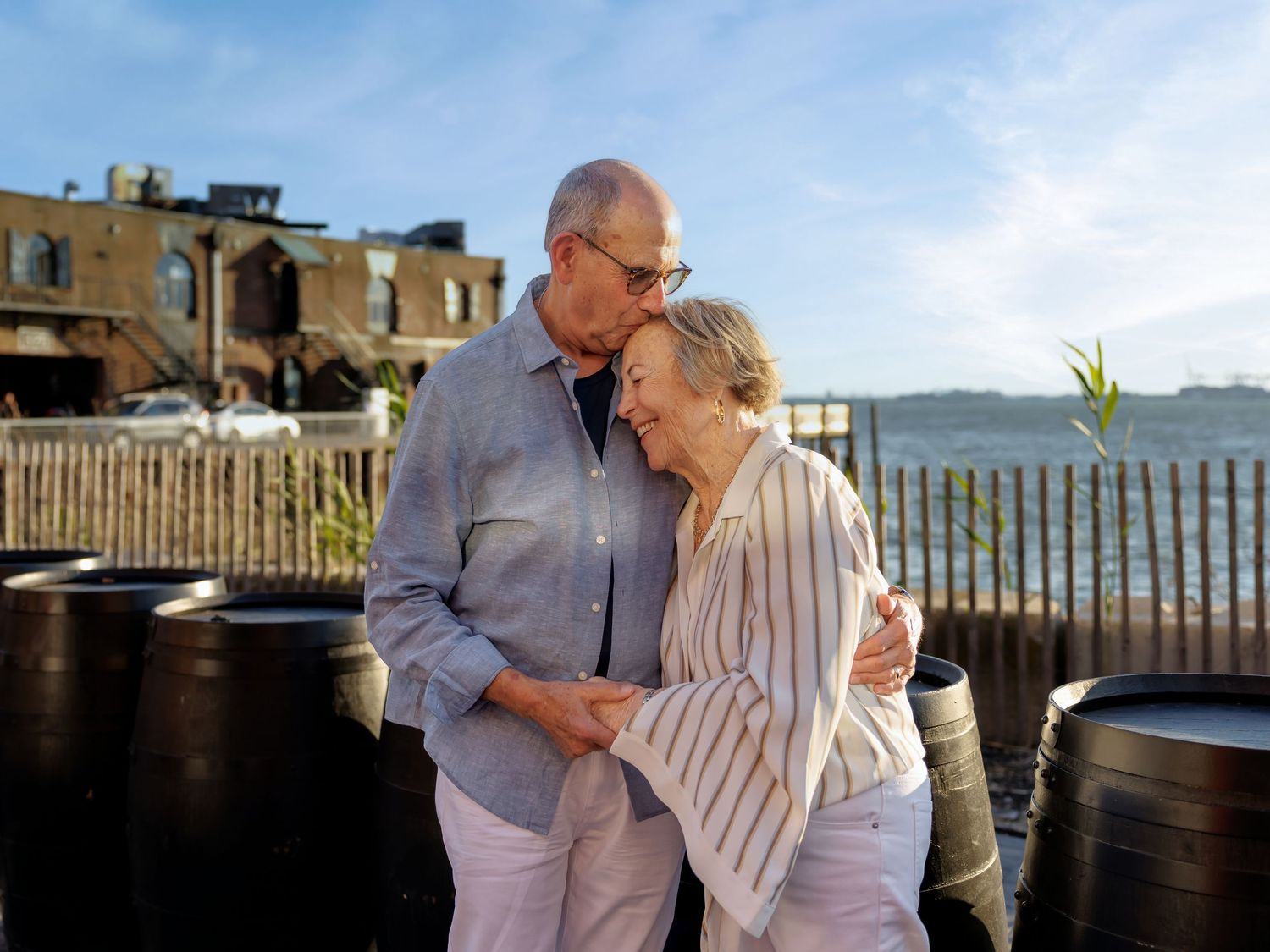 Older couple sharing a romantic moment outdoors near a waterfront venue on a sunny day.