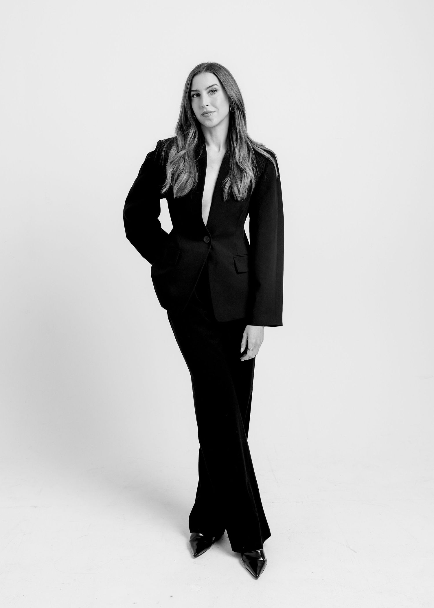 Woman in black tailored suit with wide-leg trousers, full-length black and white photo.