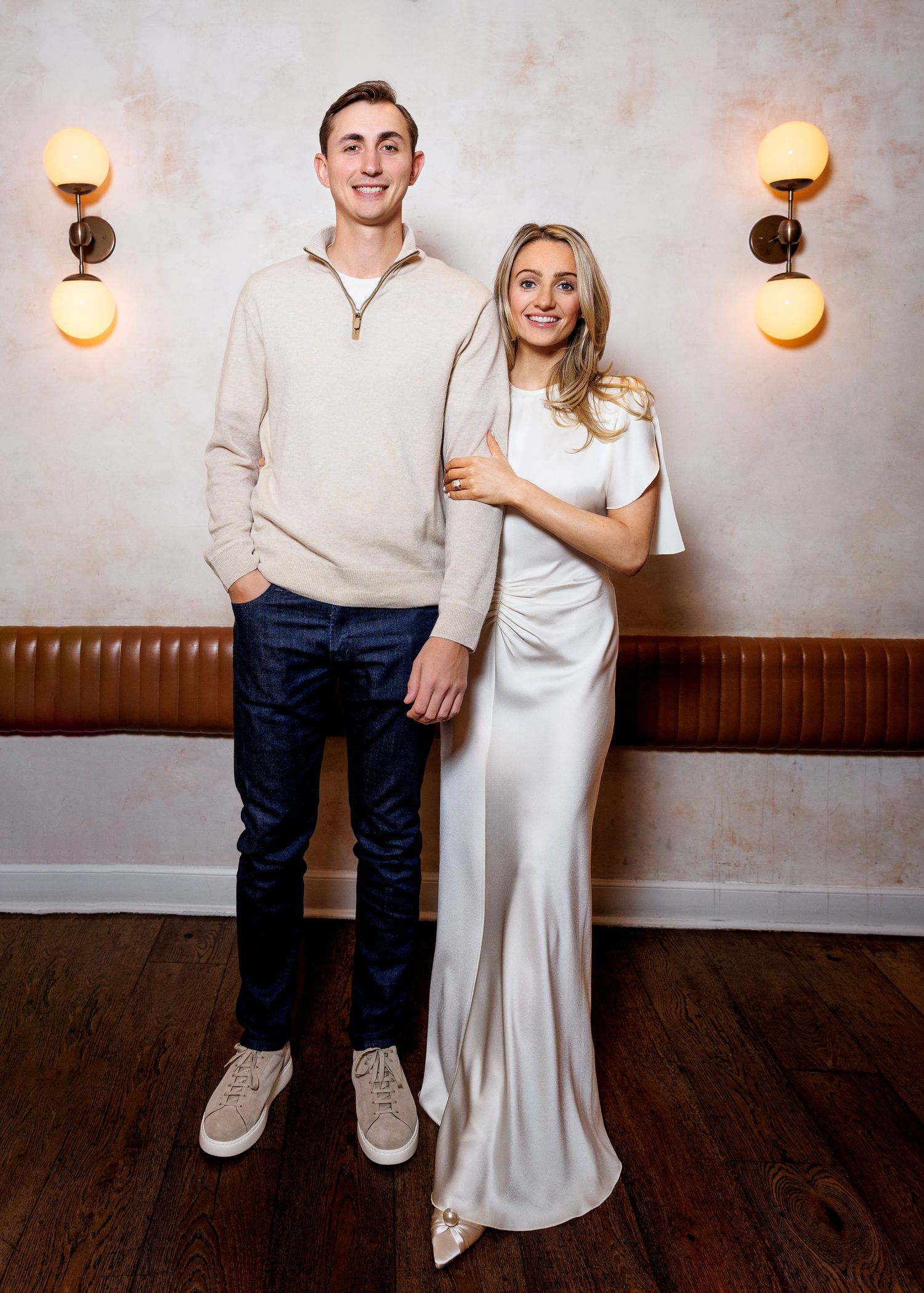 Tall man and woman in white dress posing together inside a warmly lit restaurant.
