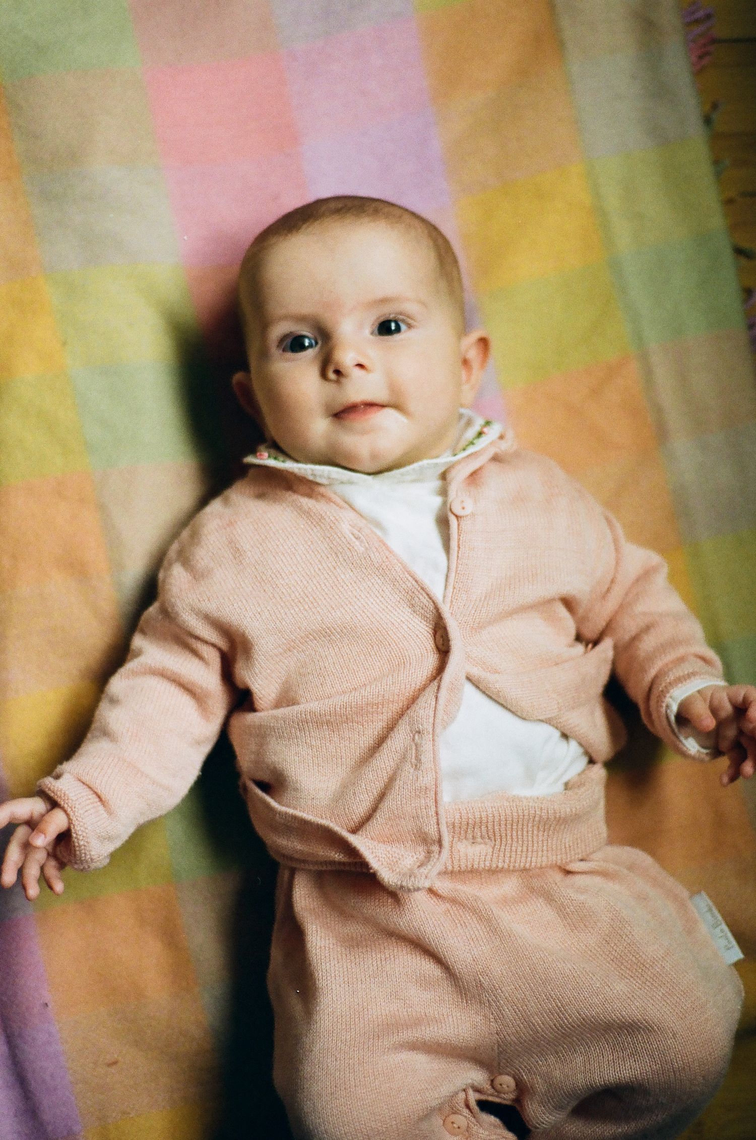 Sweet baby in pink knit outfit lying on a colorful pastel patchwork blanket.