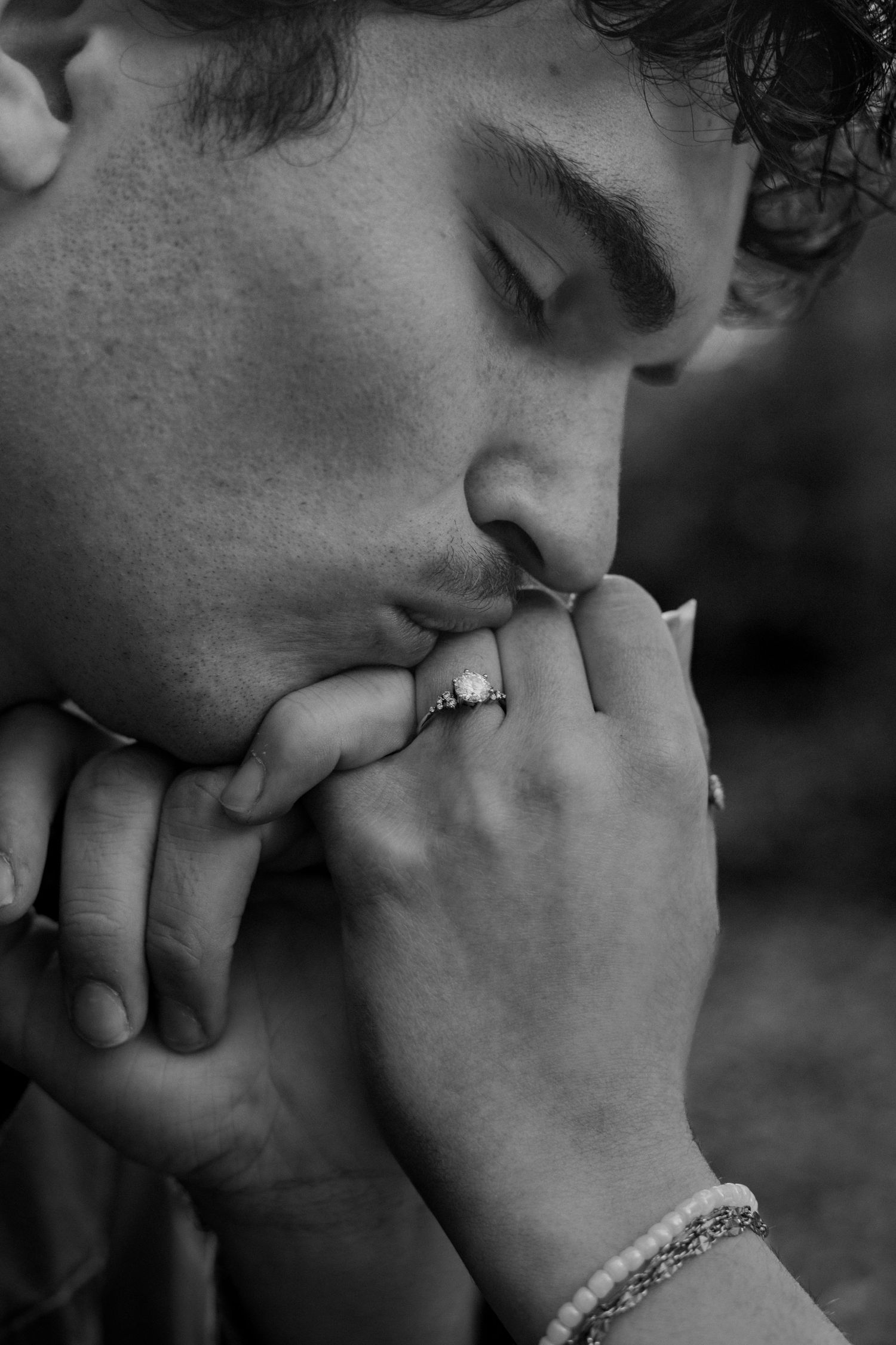 Black and white of man kissing the ringed finger of his fiancee. Close up of ring.