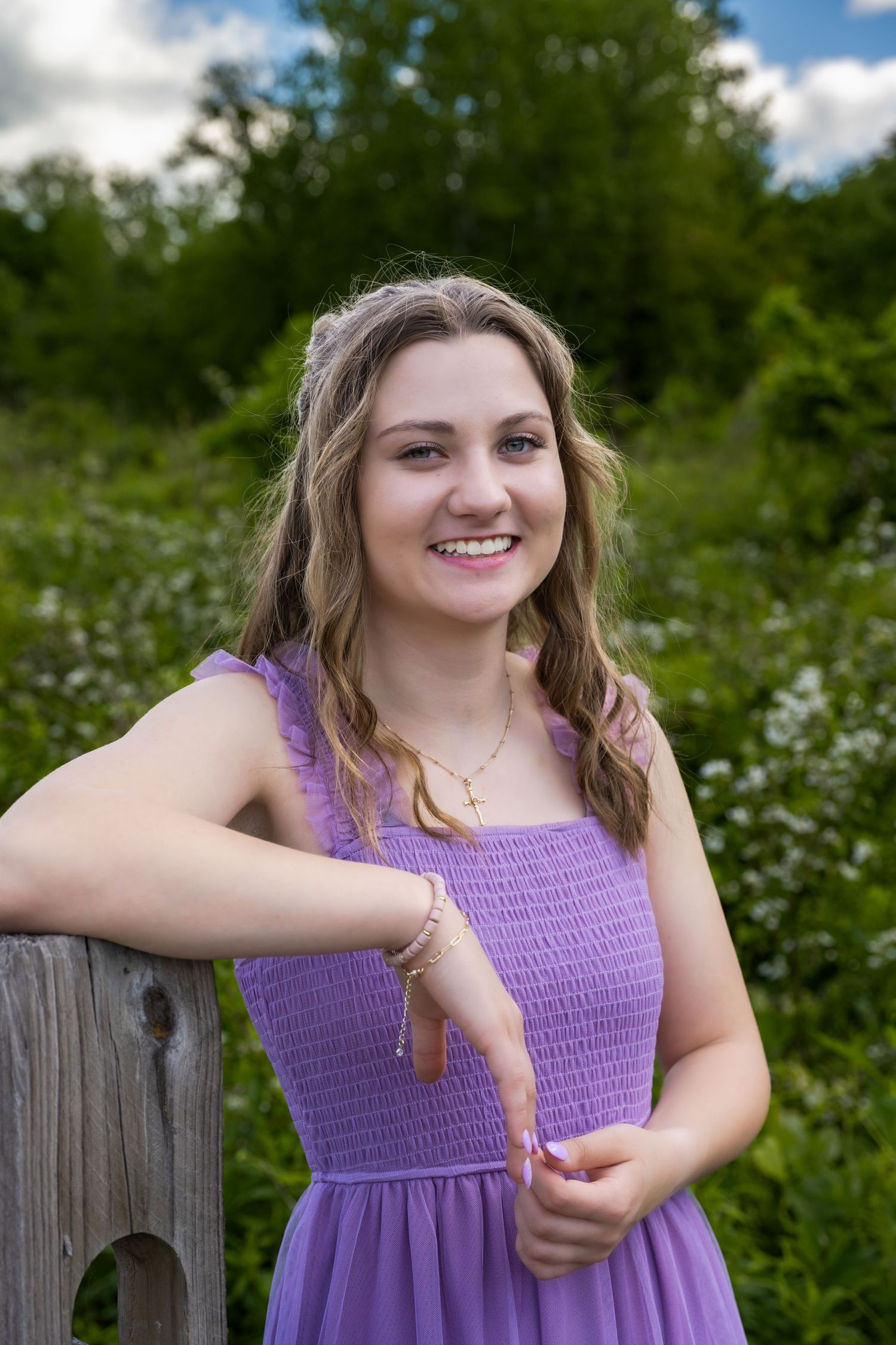 Senior girl leaning on fence post in field wearing purple dress