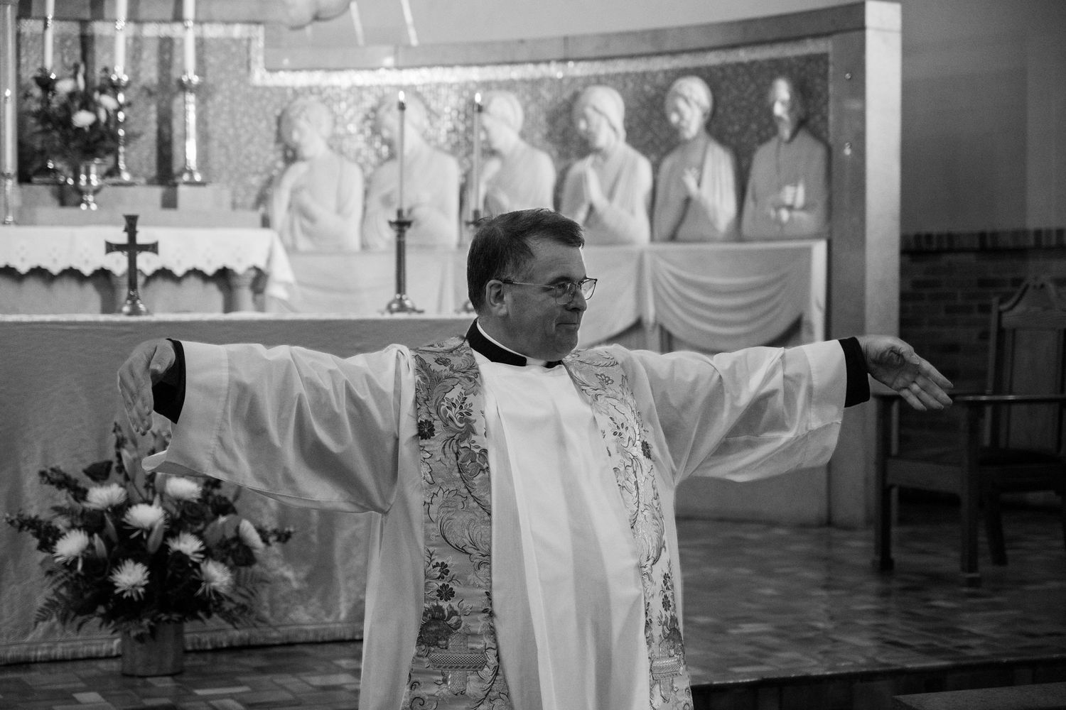 Black and white of Priest holding out arms ready to embrace Bride and Groom after wedding ceremony
