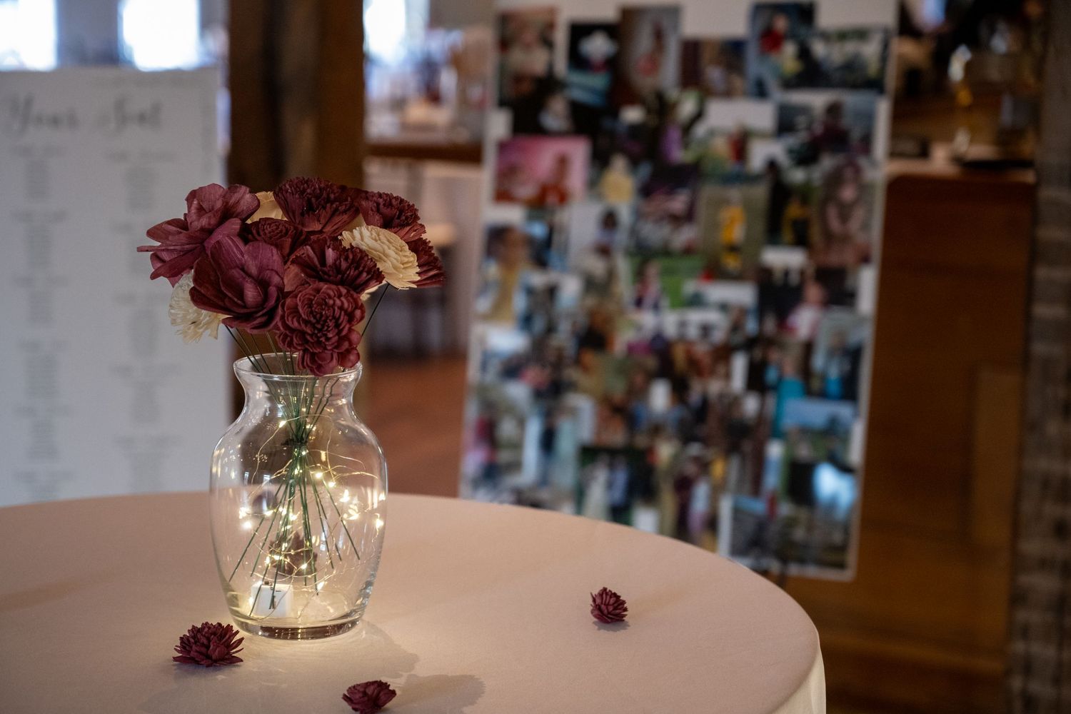 Center piece of wooden flowers with twinkle lights in the vase with seating chart and photos in the background