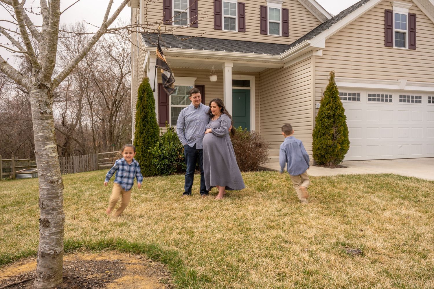 Maternity photo mom and dad standing together and children running around parents in front of their house.