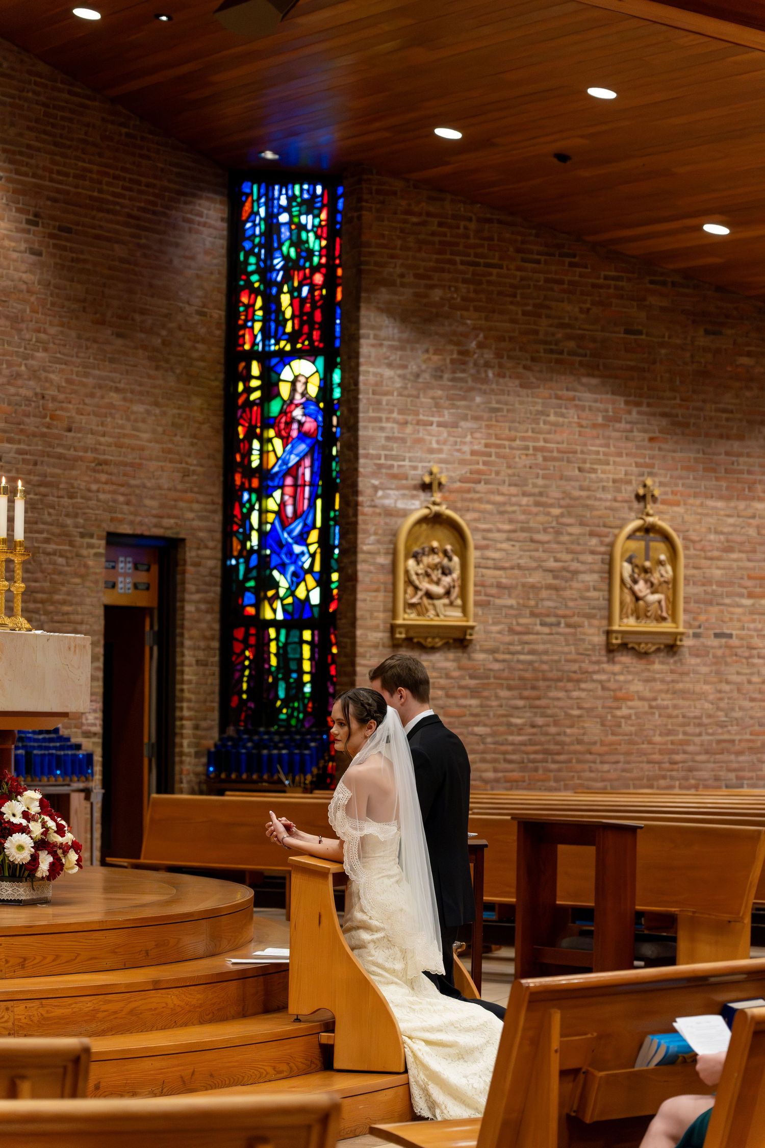 Bride & groom kneeling before alter w/stainless window in background St. Mary of the Immaculate Conception Catholic Church Fredericksburg Va