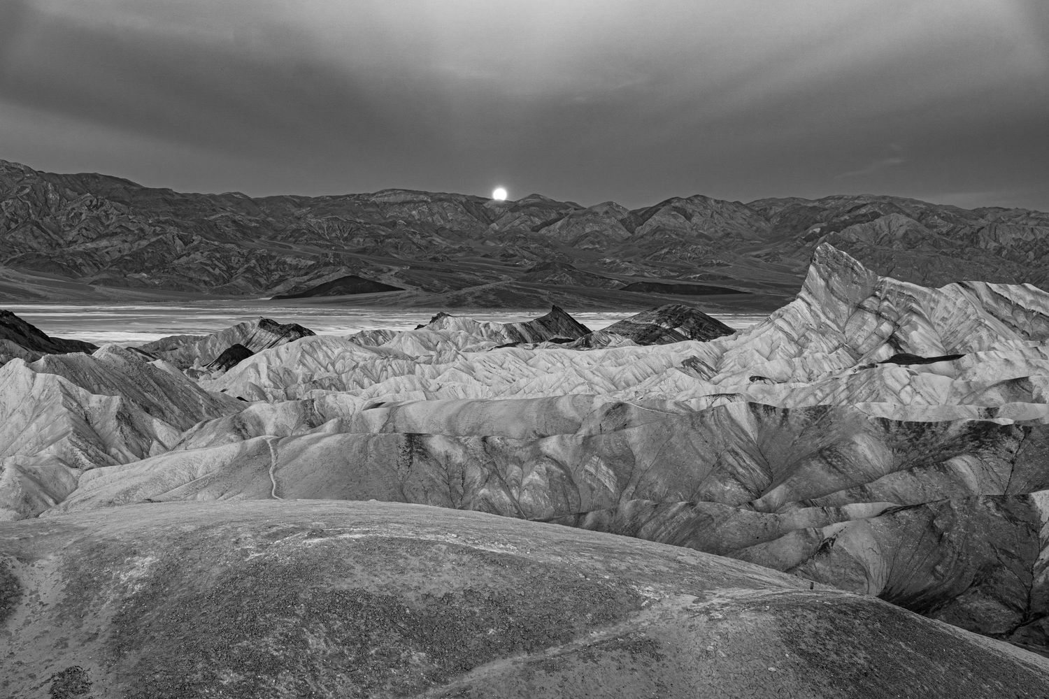 Panoramic black and white landscape photograph of rugged mountain ranges under dramatic cloudy skies.
