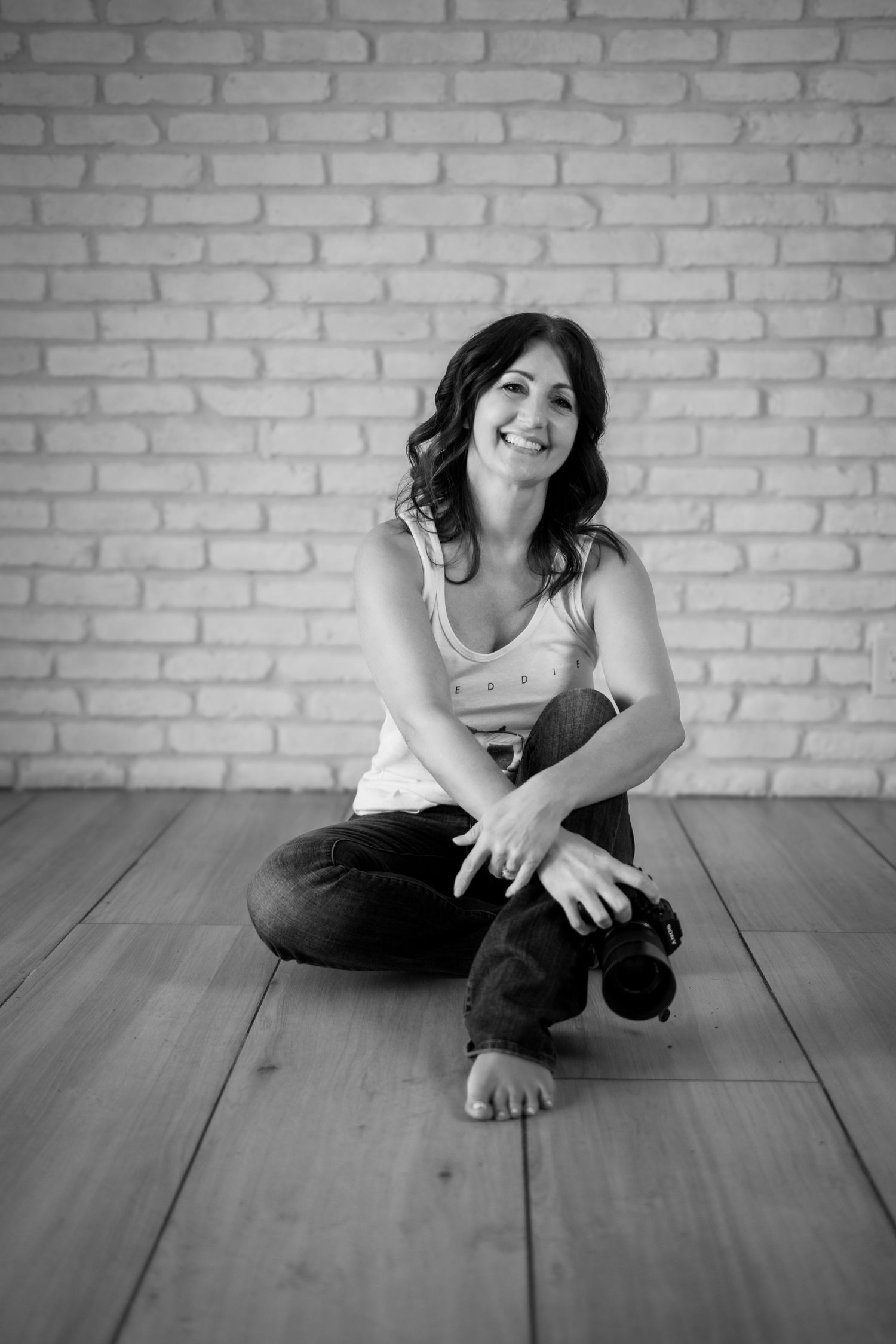 Black and white portrait series against brick wall showing playful poses on wooden floor.
