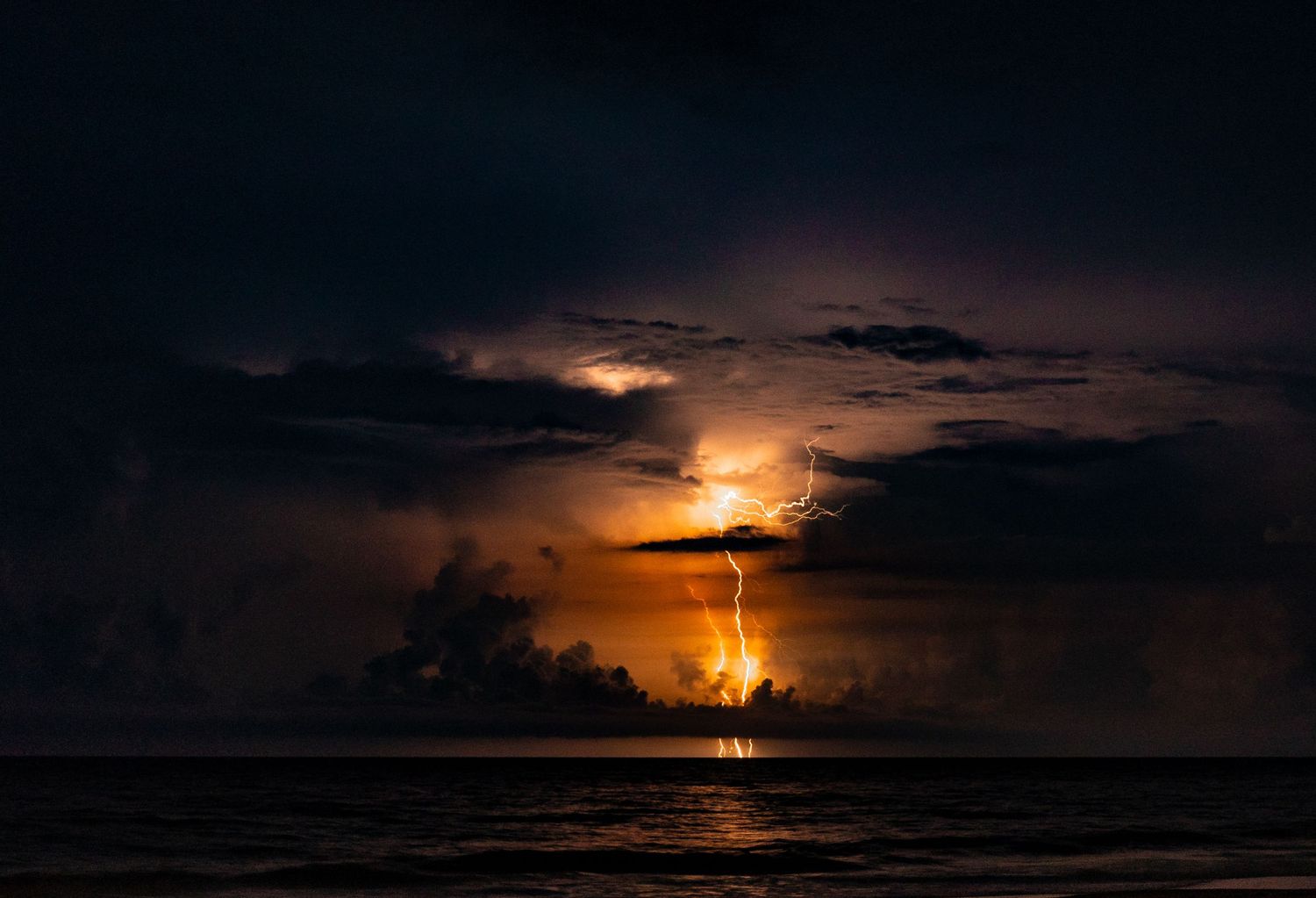 Lightning bolts flash across a moody sunset seascape with stormy clouds.