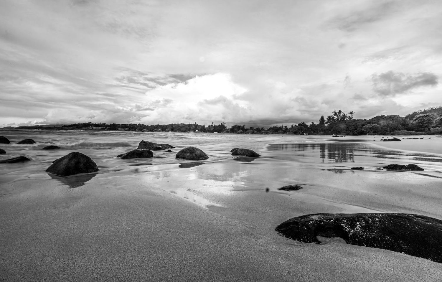 Panoramic view of rocky coastline with dramatic clouds reflecting in tidal pools at low tide.