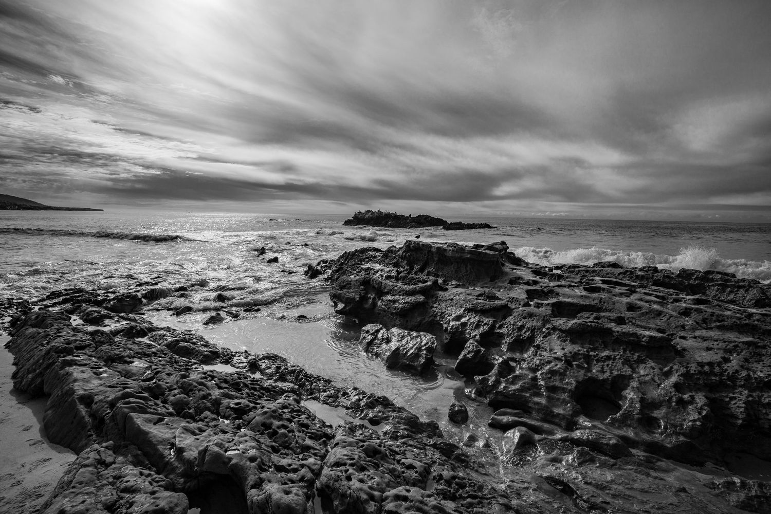 Rocky coastal landscape with dramatic clouds and rugged cliffs extending into the distance.