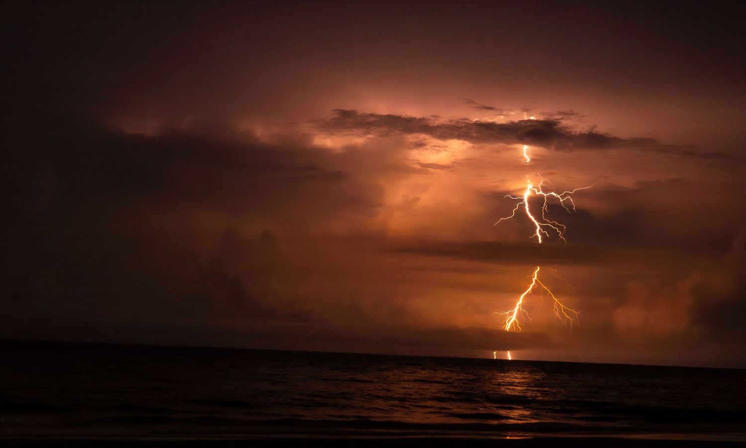 Dramatic panorama of lightning strikes over an ocean at sunset.