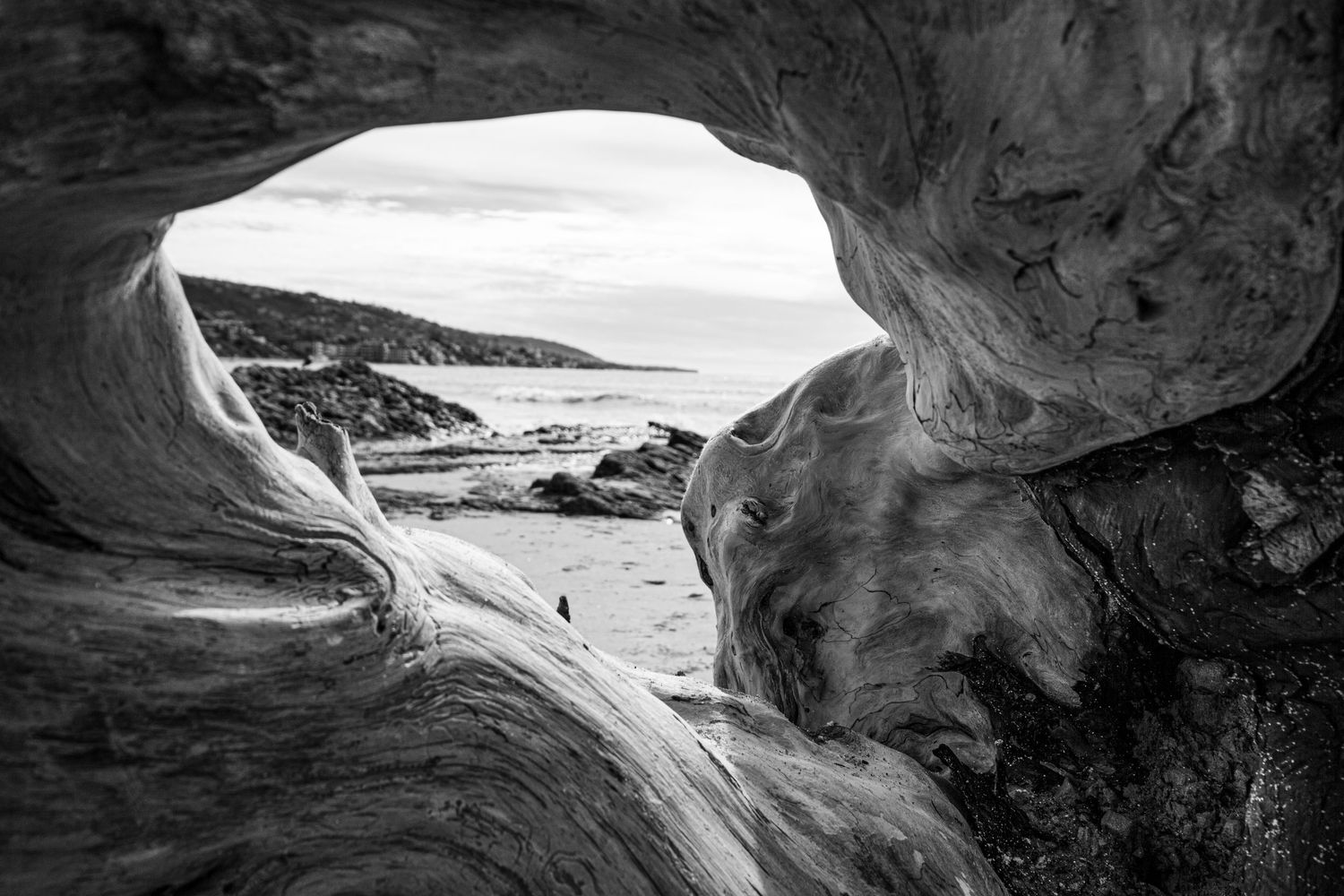Black and white view of ocean coastline framed through a natural rock arch formation.
