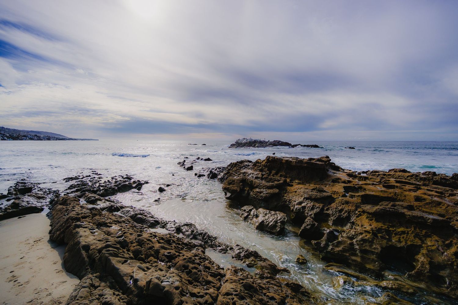 Rocky coastal landscape with waves crashing against rugged cliffs under cloudy skies.