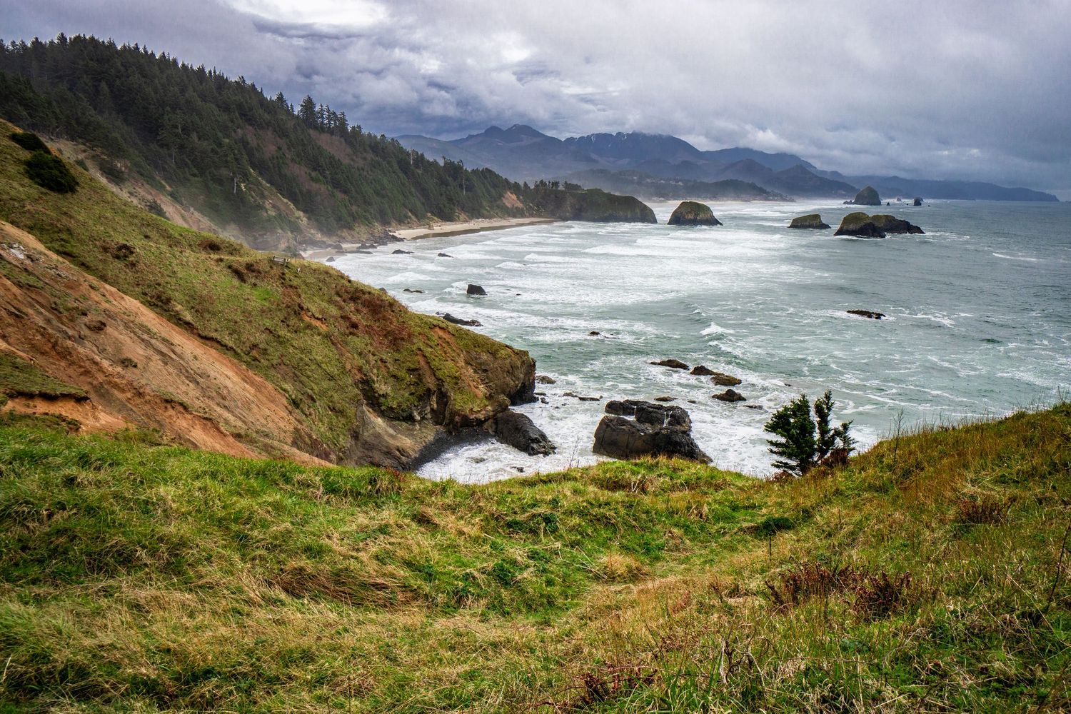 Scenic Oregon coast viewpoint overlooking mountains, beaches and sea stacks with moody overcast skies.