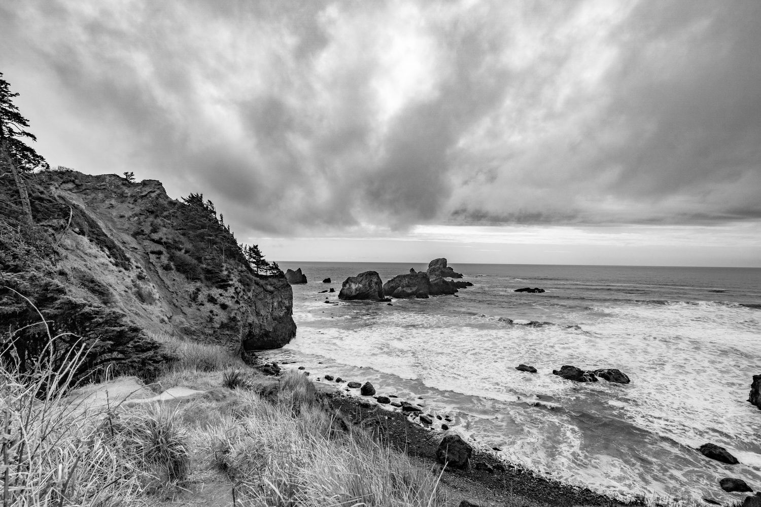 A dramatic black and white panoramic view of a rugged coastal landscape with rocky cliffs and stormy clouds overhead.
