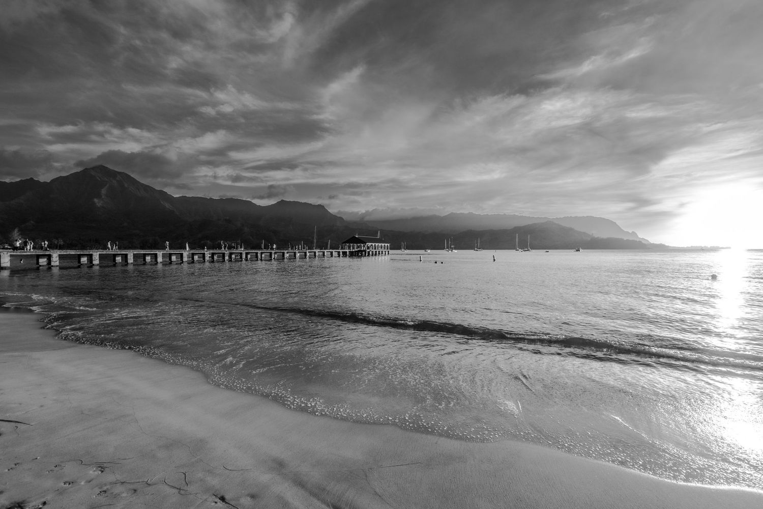 Coastal sunset view with long pier extending into the ocean and mountains in the background.