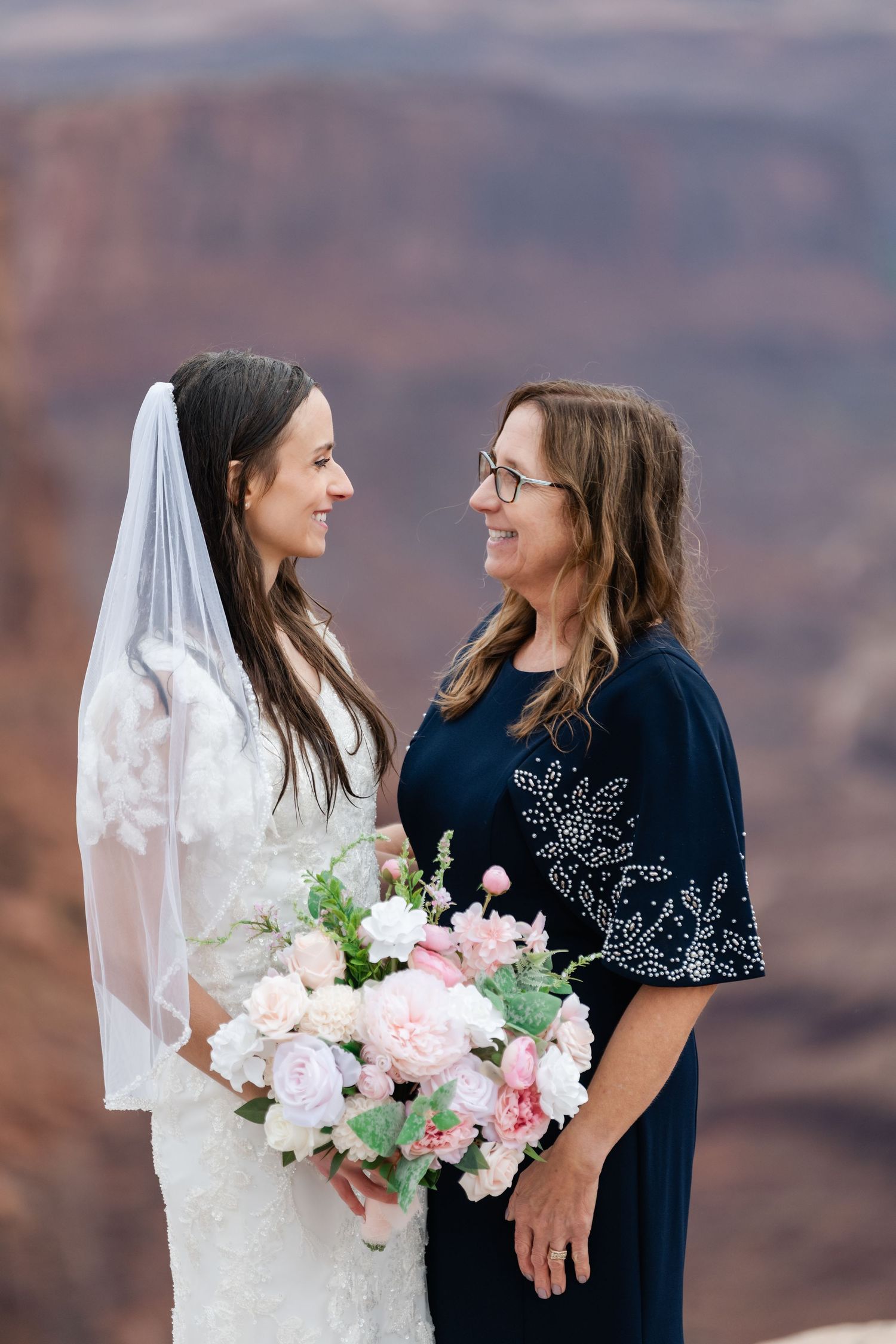 Two people sharing joyful moments while holding pink and white flower bouquets against a desert landscape.