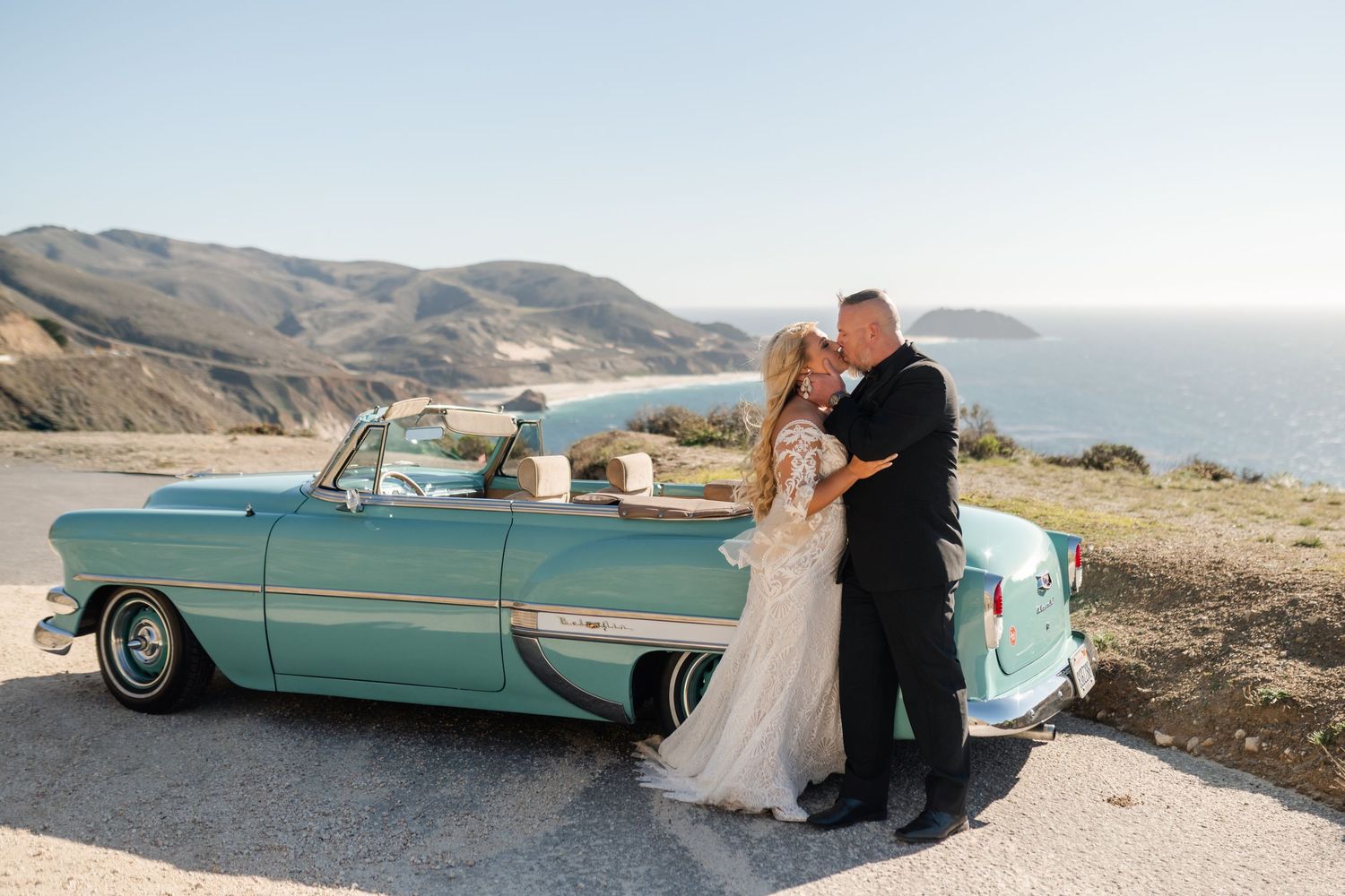 A classic mint green convertible car parked along a scenic coastal cliff during sunset.