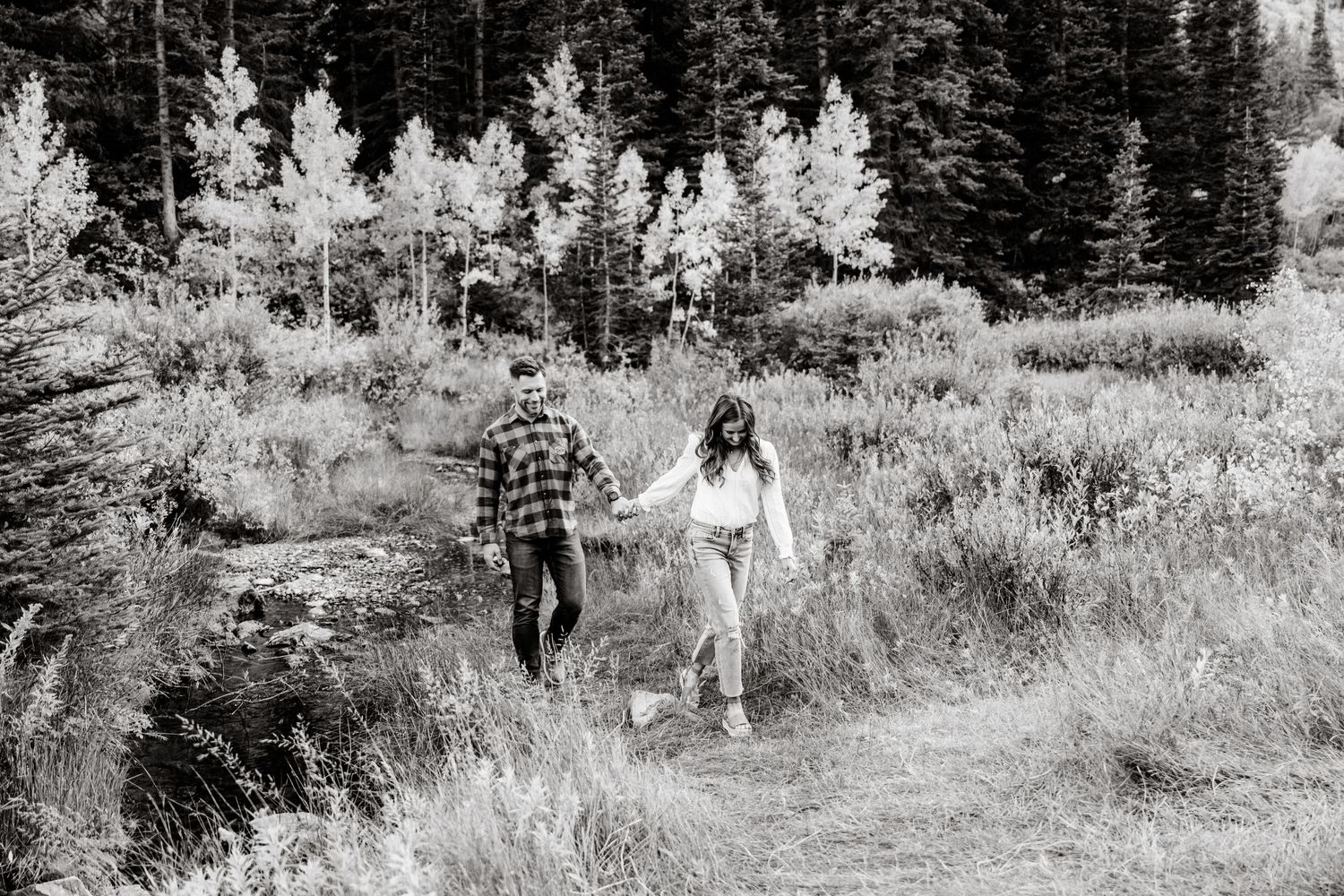 A couple walking hand in hand along a wooded trail in a forest setting.