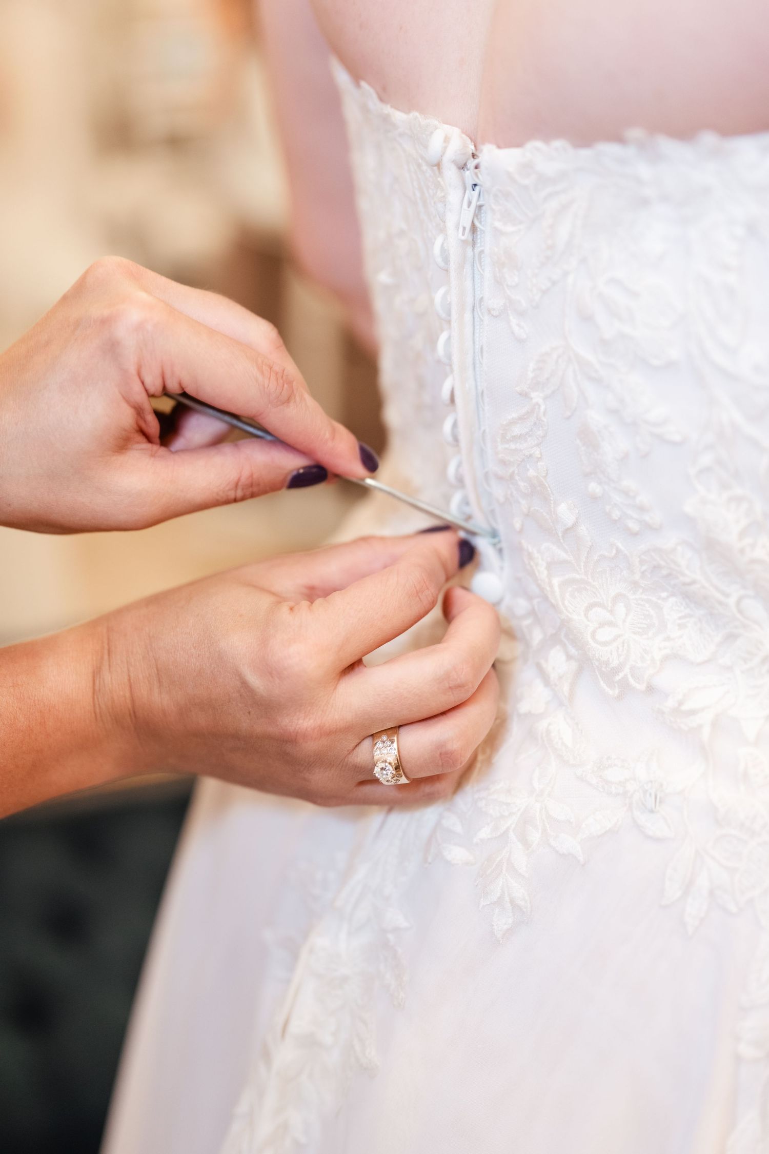 Hands lacing up an intricate white lace wedding dress corset while wearing an engagement ring.