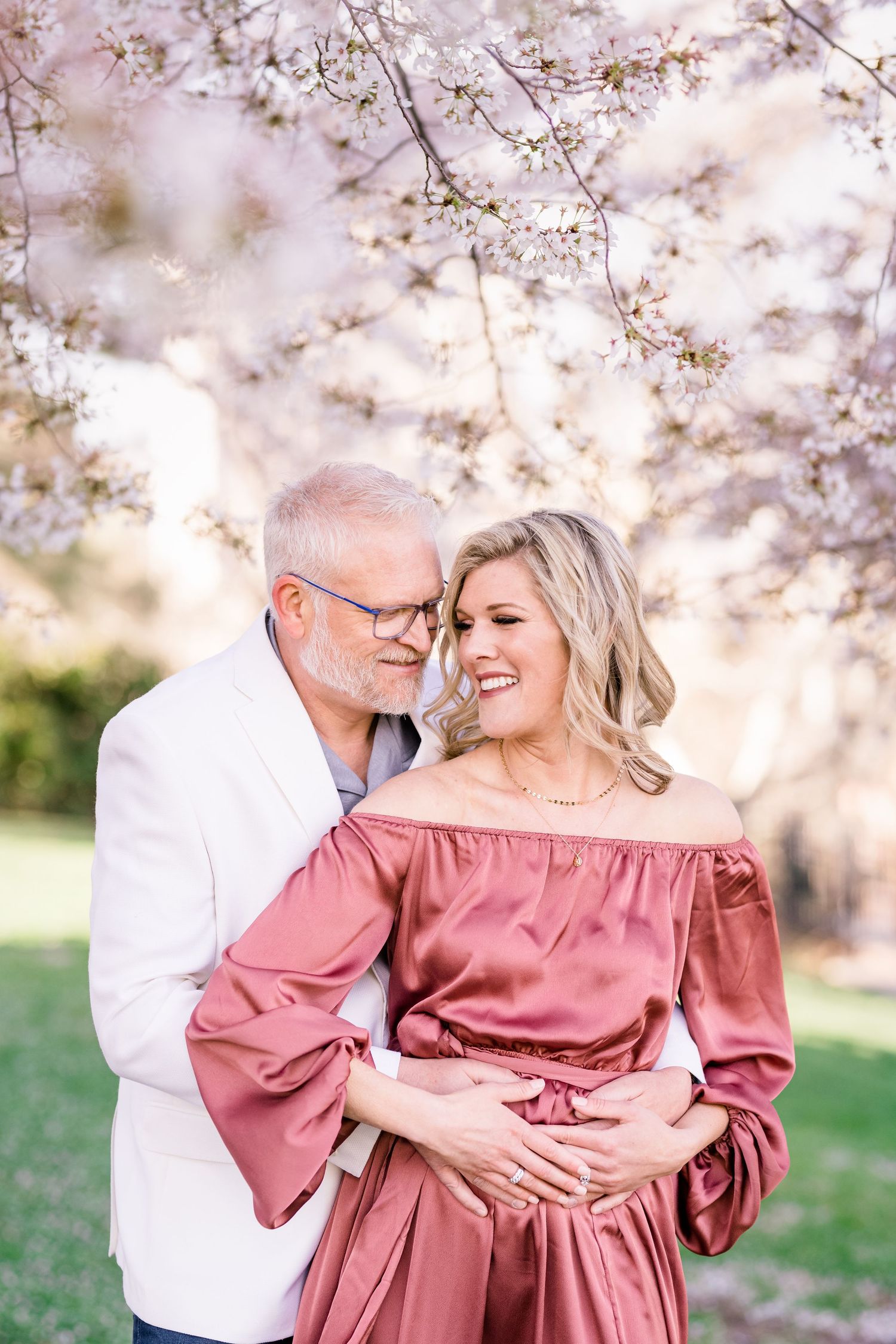 engaged couple cuddling under the cherry blossoms by timeless wedding photographer