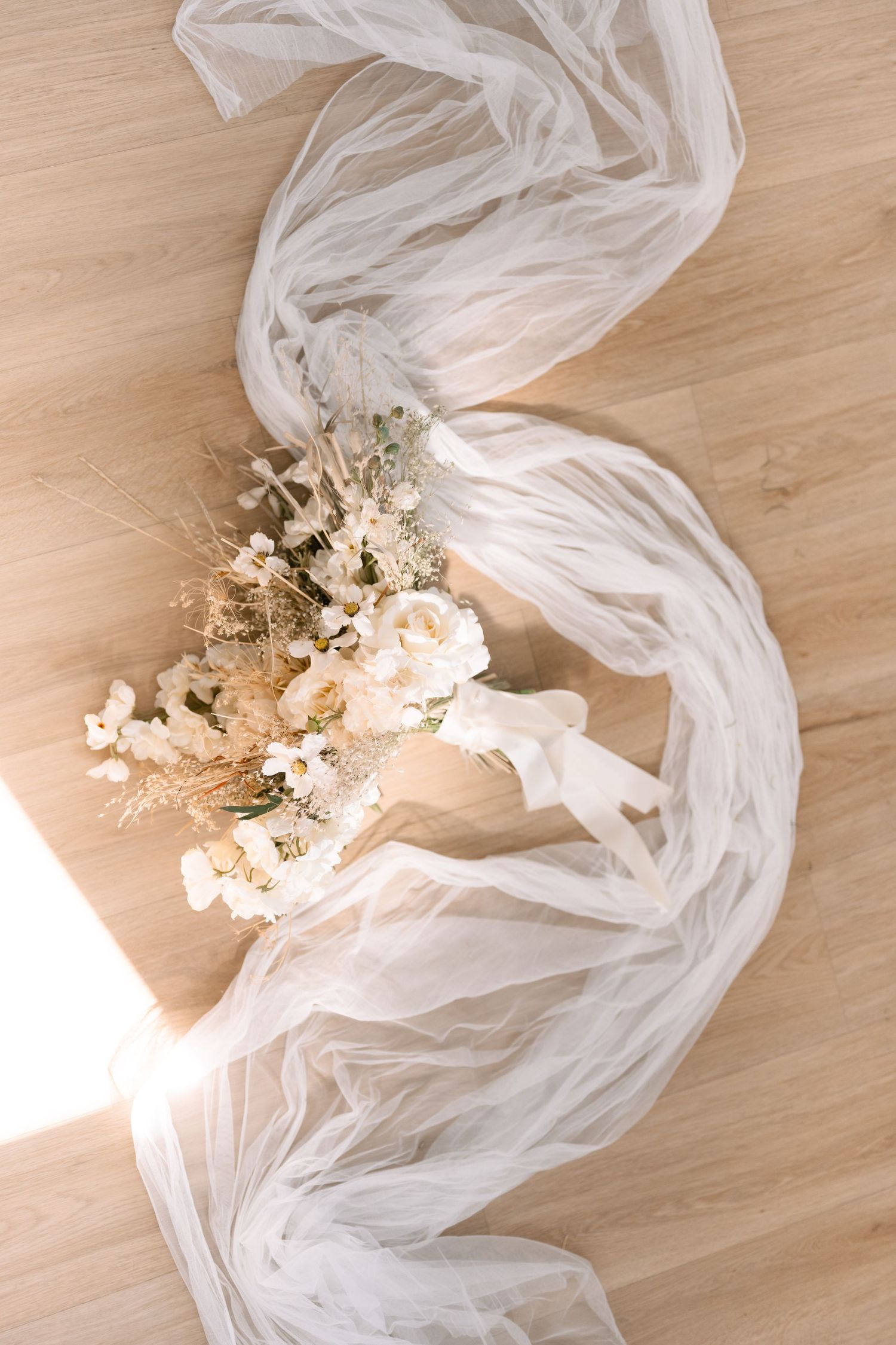 Ethereal bridal veil with dried floral arrangement on wooden floor.