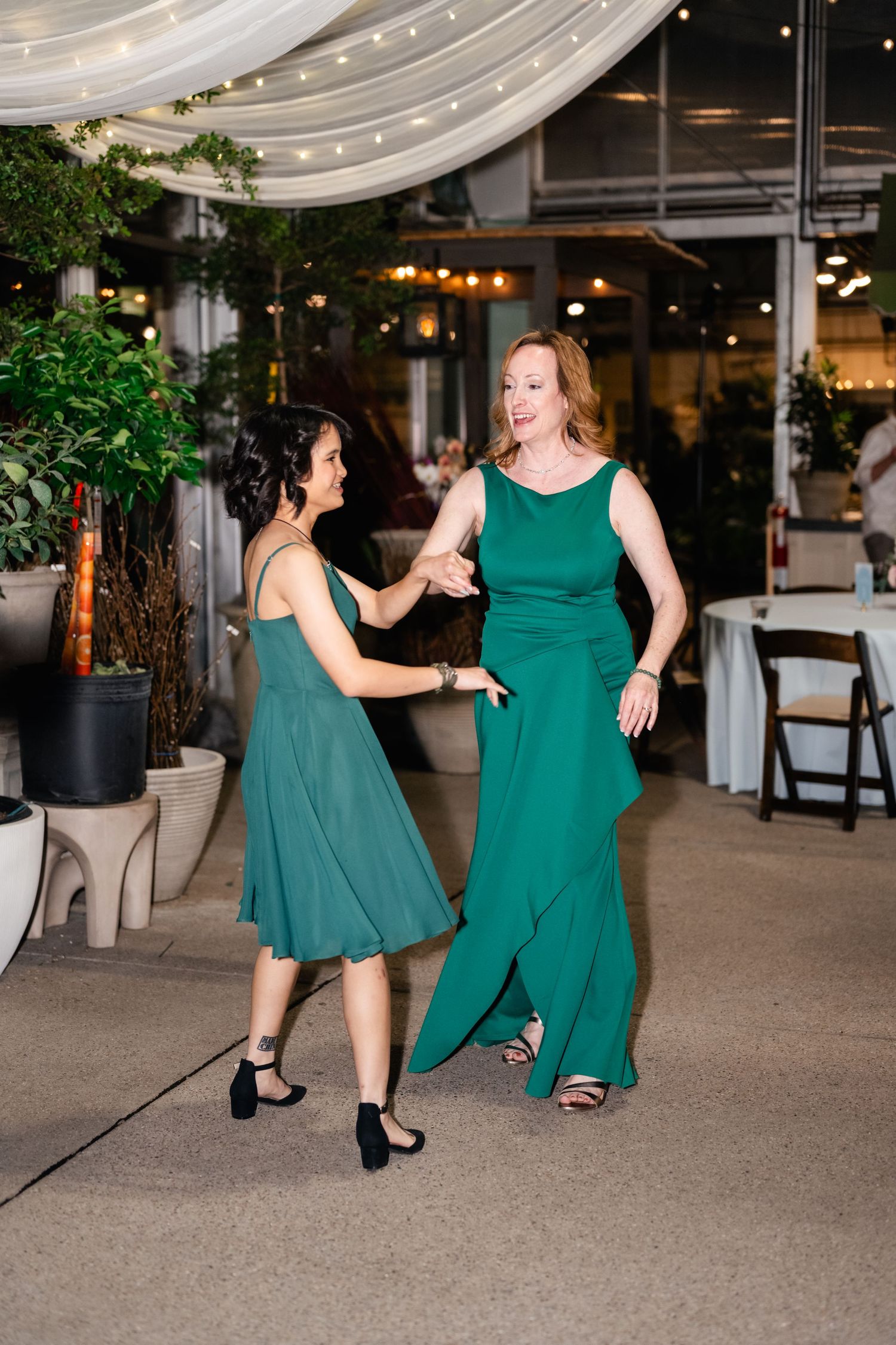 People dance together during a reception in an elegant venue decorated with white drapes and greenery.