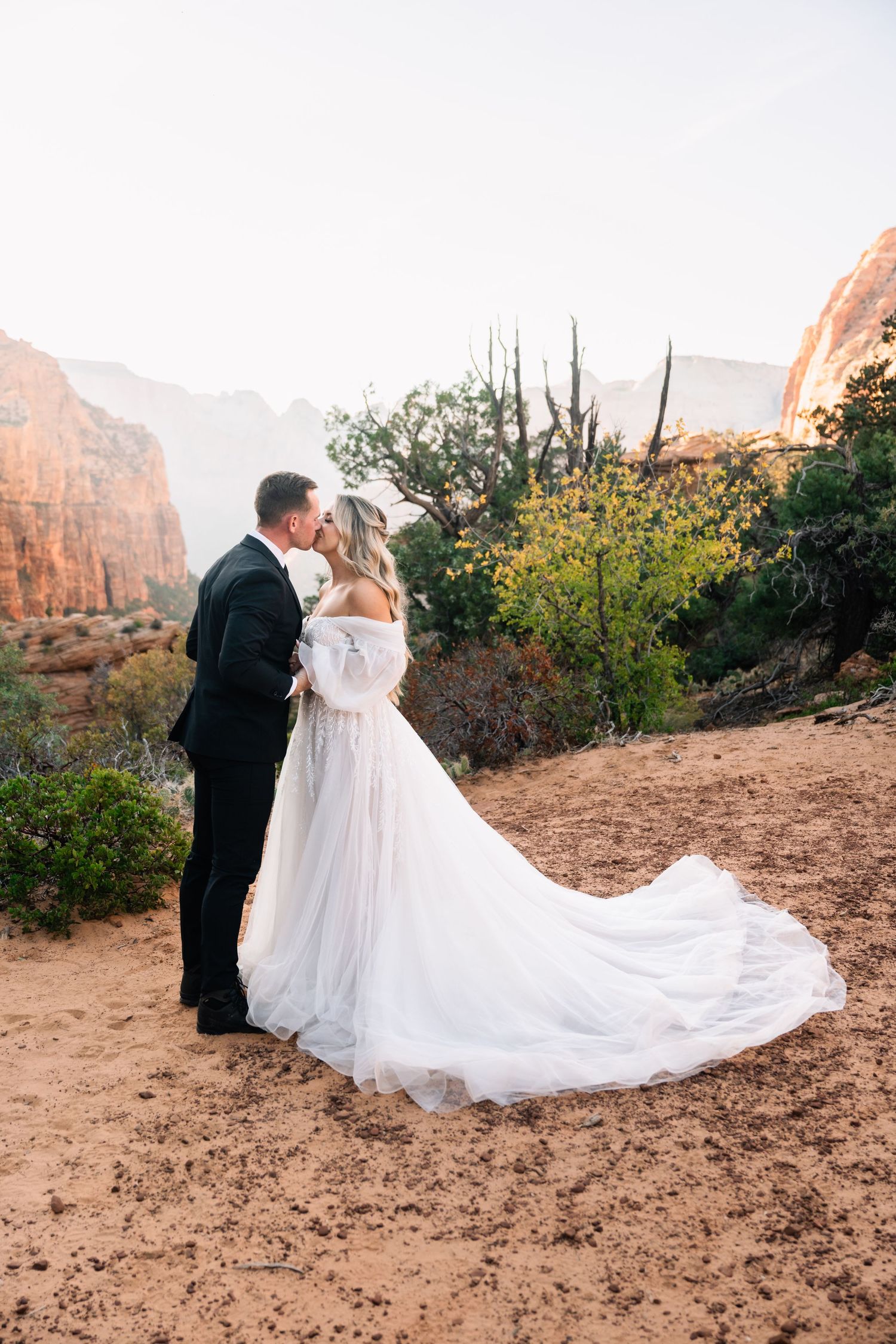 Elegant wedding dress train flows across desert landscape with towering red cliffs.
