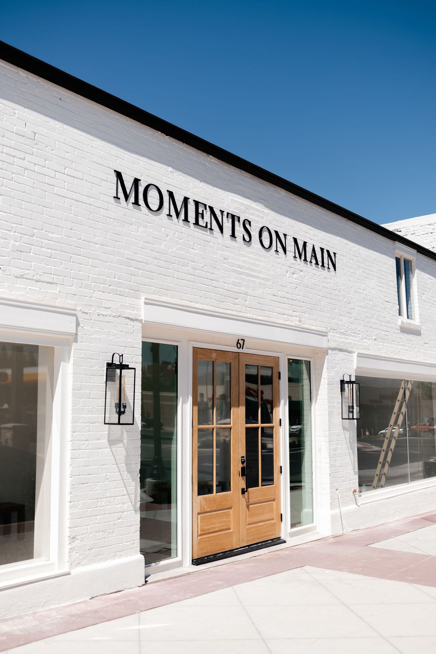 Modern white brick retail building facade with wooden doors and large windows displaying 