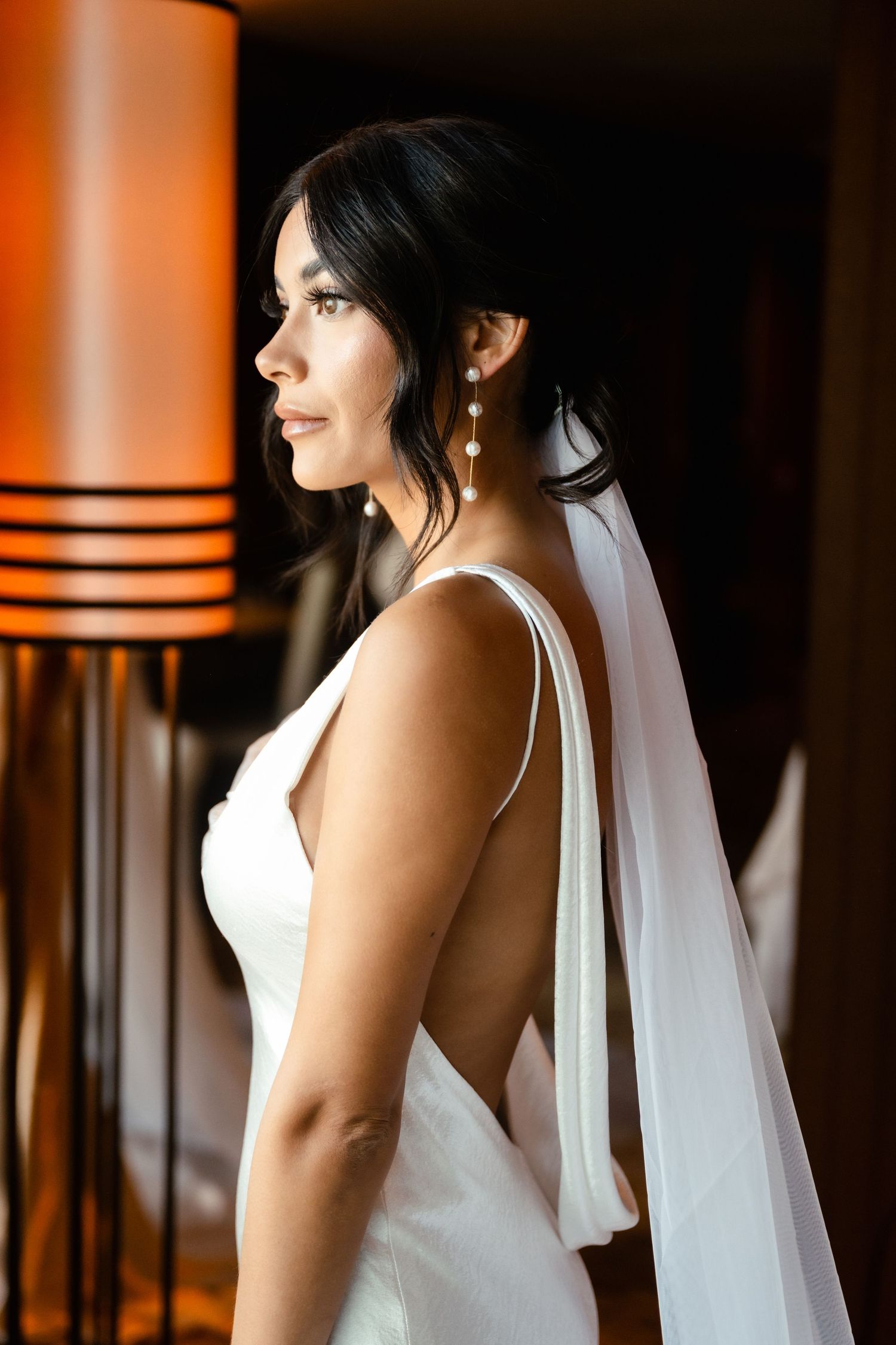 Bride in white wedding dress with flowing veil standing in dramatic lighting.